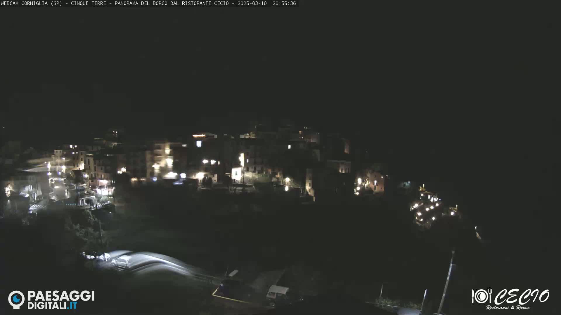 A nighttime, high-angle view shows a small, hilly town with scattered lights, under a dark, clear sky.