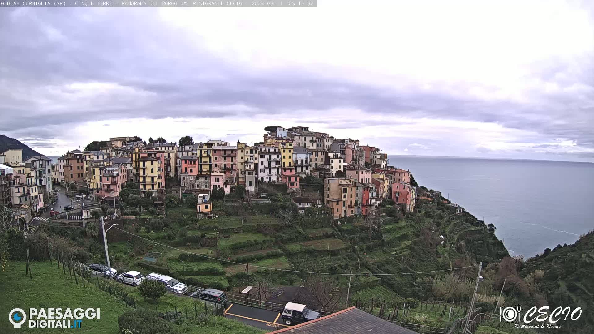 A colorful hillside village overlooks a calm ocean under a cloudy sky.