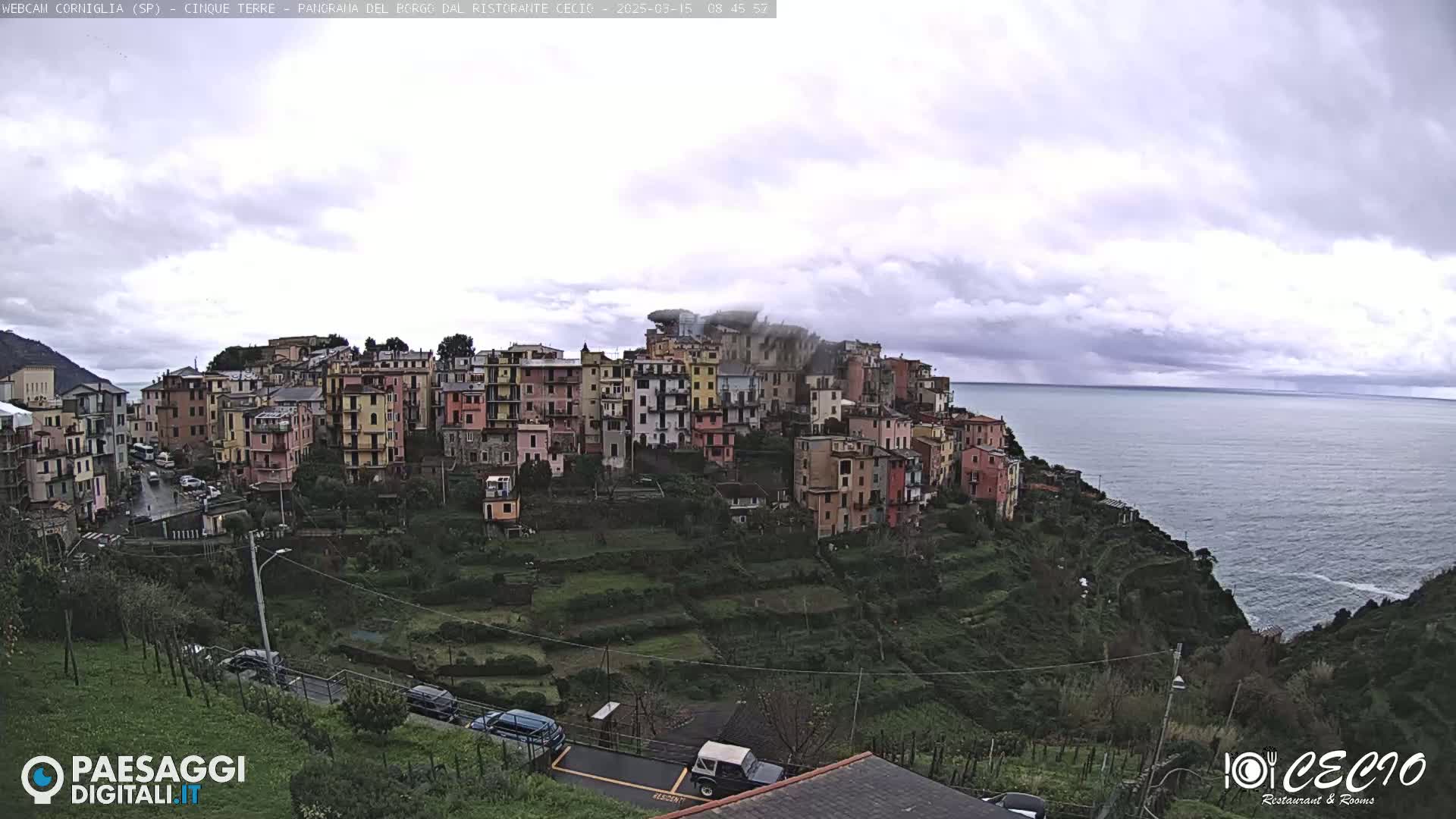 A coastal town of colorful buildings on a hillside overlooking a calm sea under a cloudy sky.