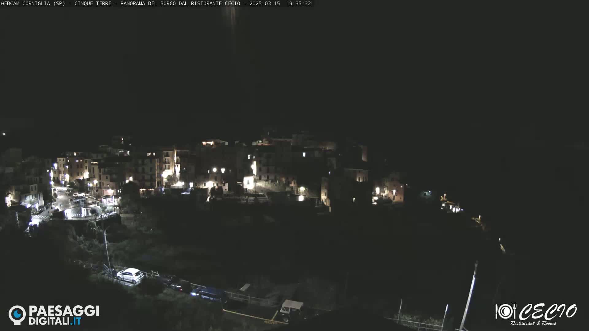 A nighttime, high-angle view of a small, illuminated town nestled into a dark hillside.