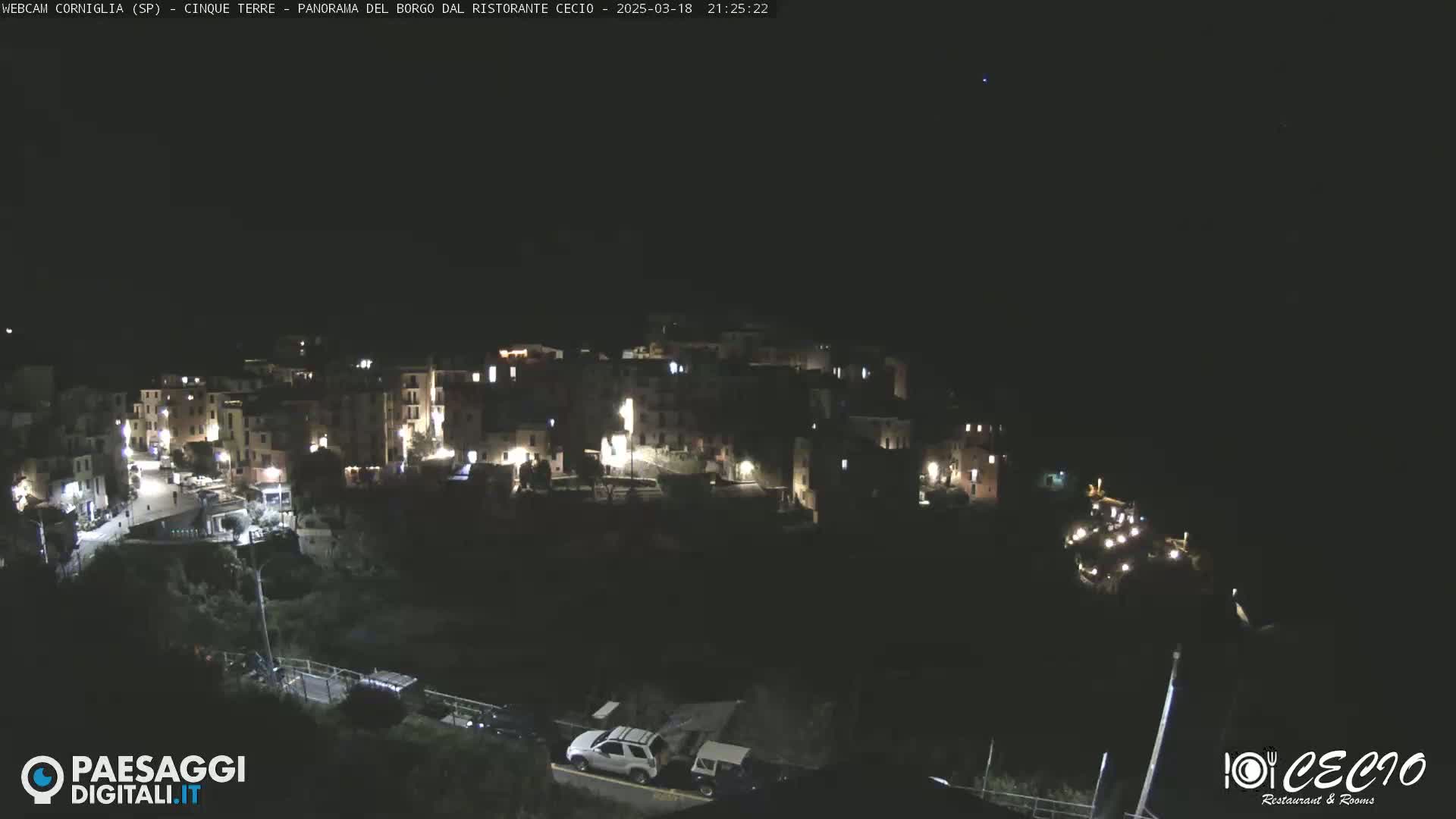 A nighttime view of a small, illuminated town nestled into a hillside under a clear, dark sky.