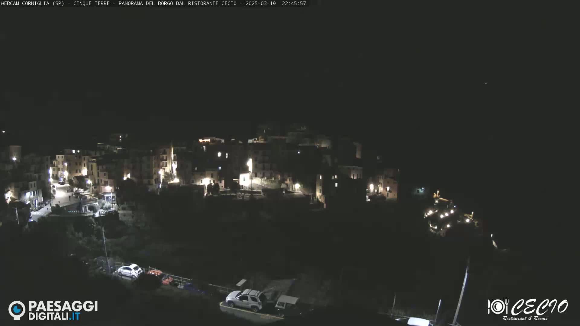 A nighttime, high-angle view of a small, illuminated village nestled on a hillside.