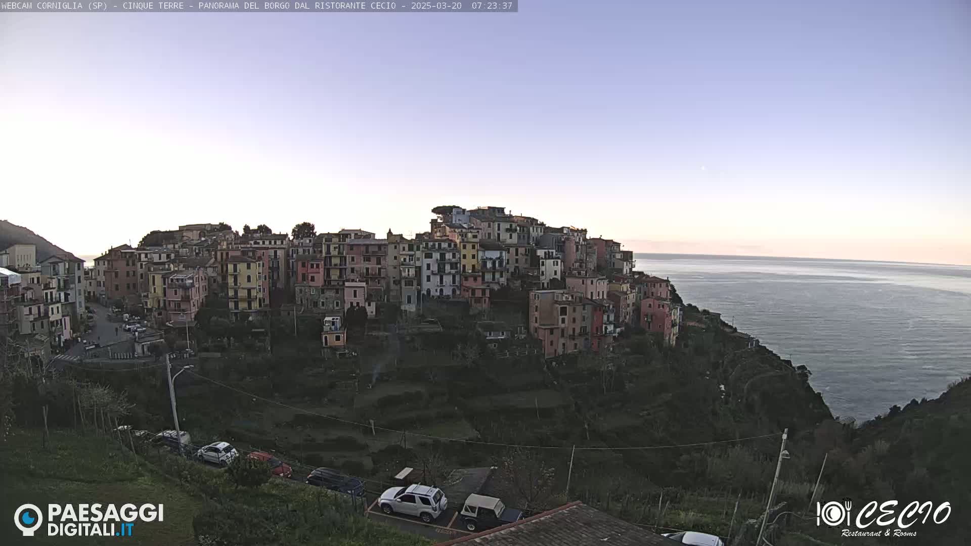 A colorful hillside village overlooks a calm sea under a clear, twilight sky.