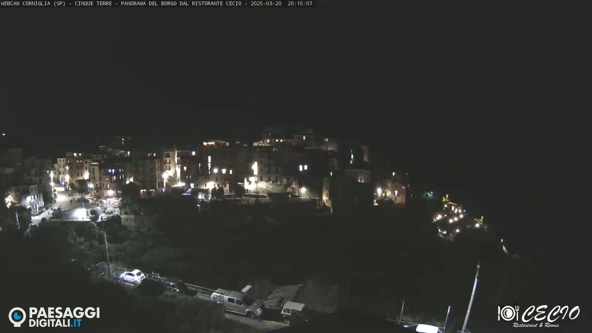 A nighttime, high-angle view shows a small, illuminated village nestled on a hillside.