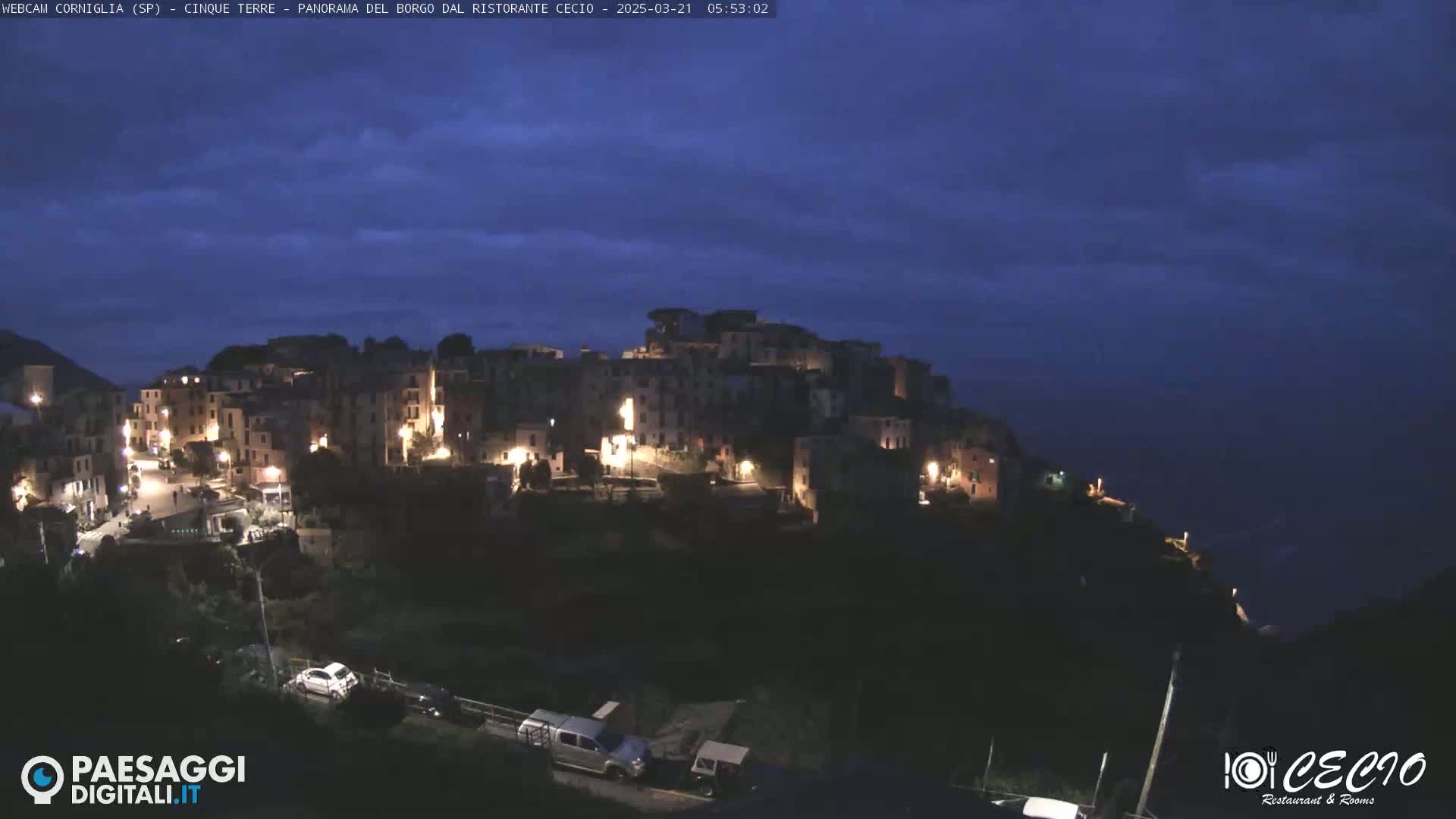 A hillside village is illuminated at night under a dark blue, twilight sky.