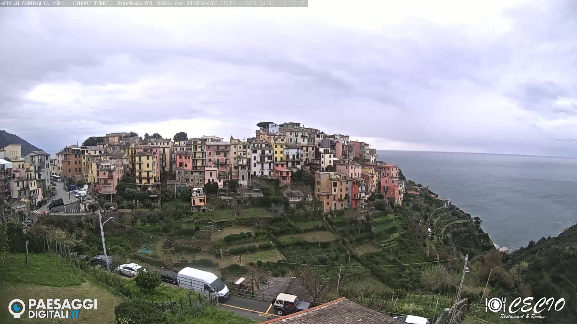 A coastal village of colorful buildings on a hillside overlooks a calm sea under an overcast sky.