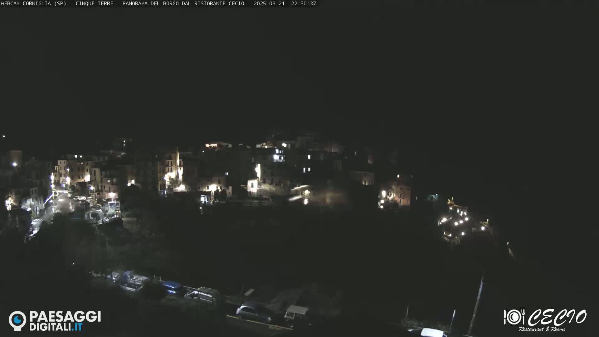 A nighttime, aerial view of a small, illuminated village nestled on a hillside.