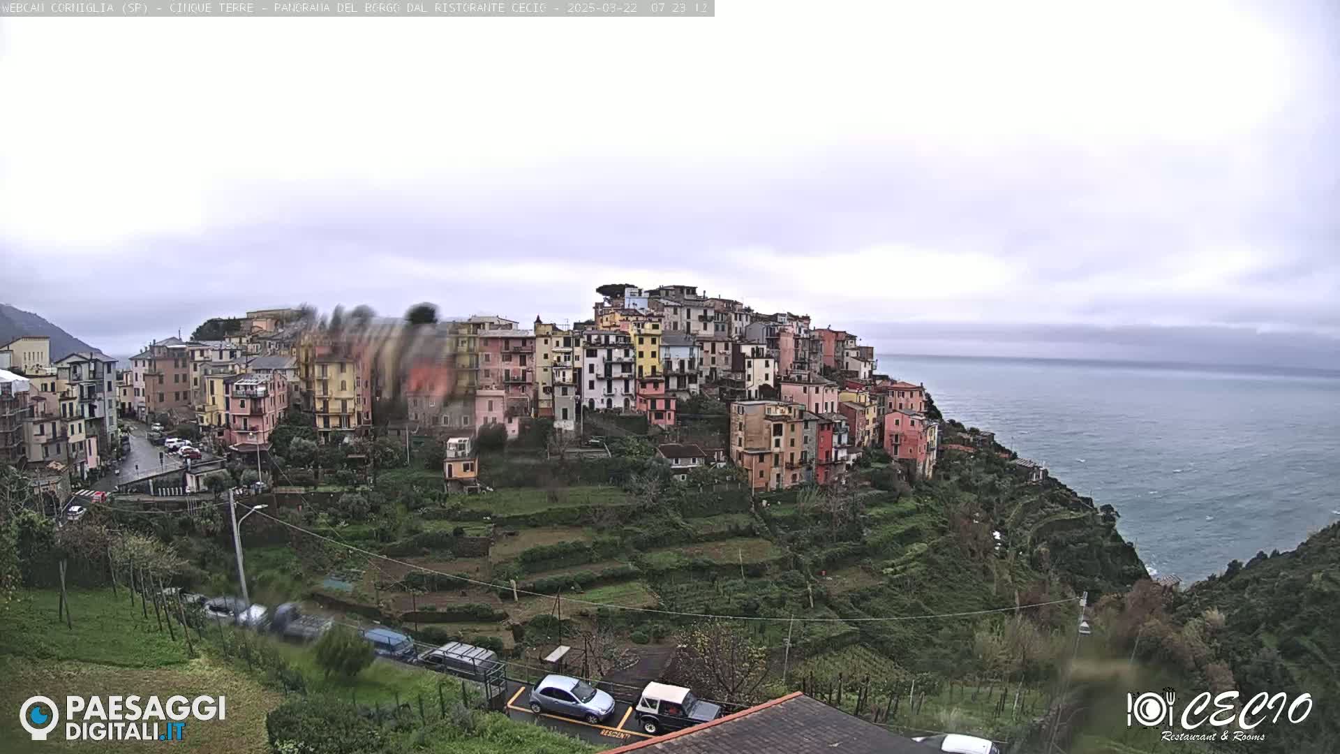 A colorful hillside village overlooks a choppy sea under an overcast sky.
