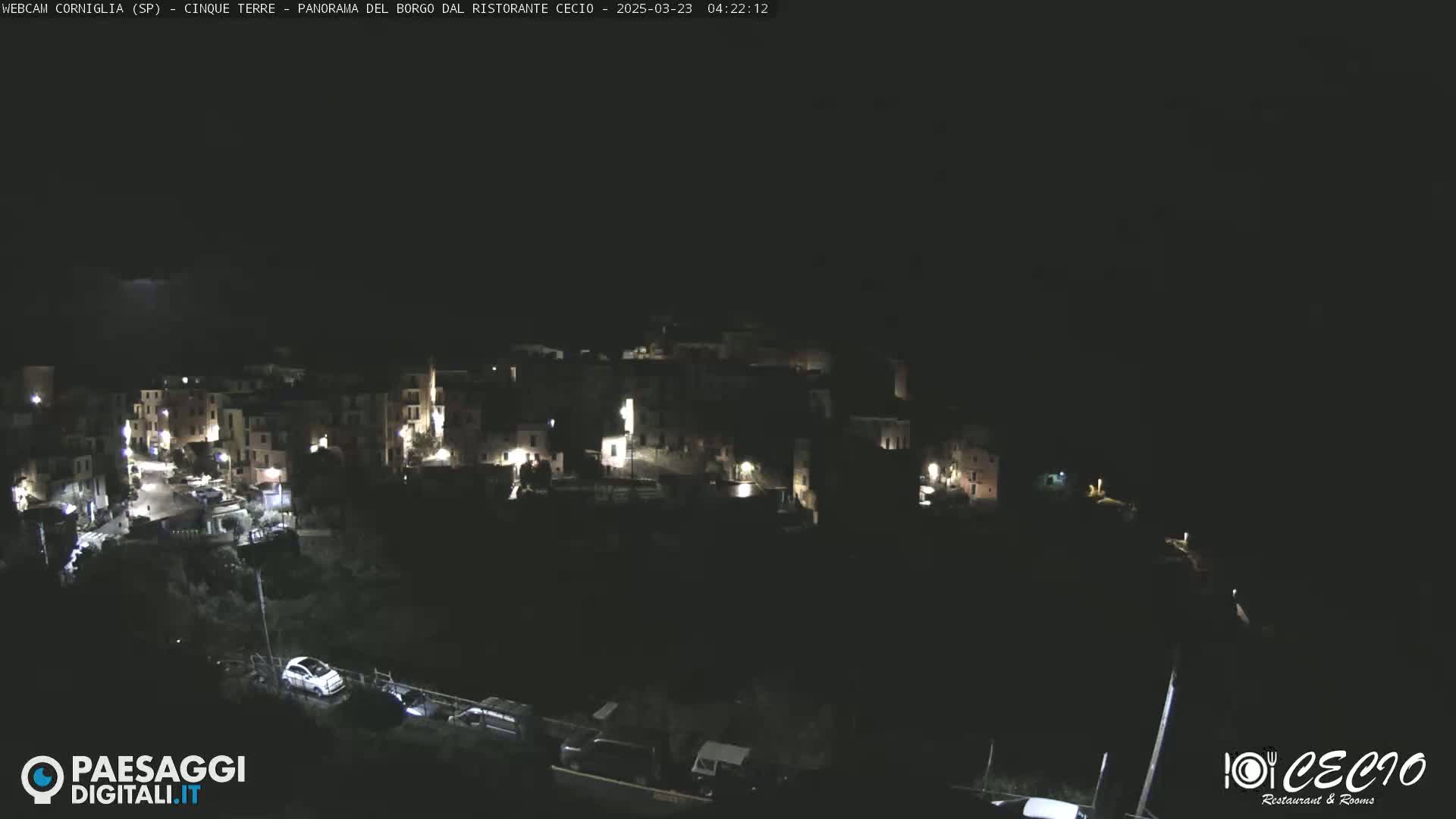 A nighttime, high-angle view shows a small, dimly lit town nestled on a hillside.
