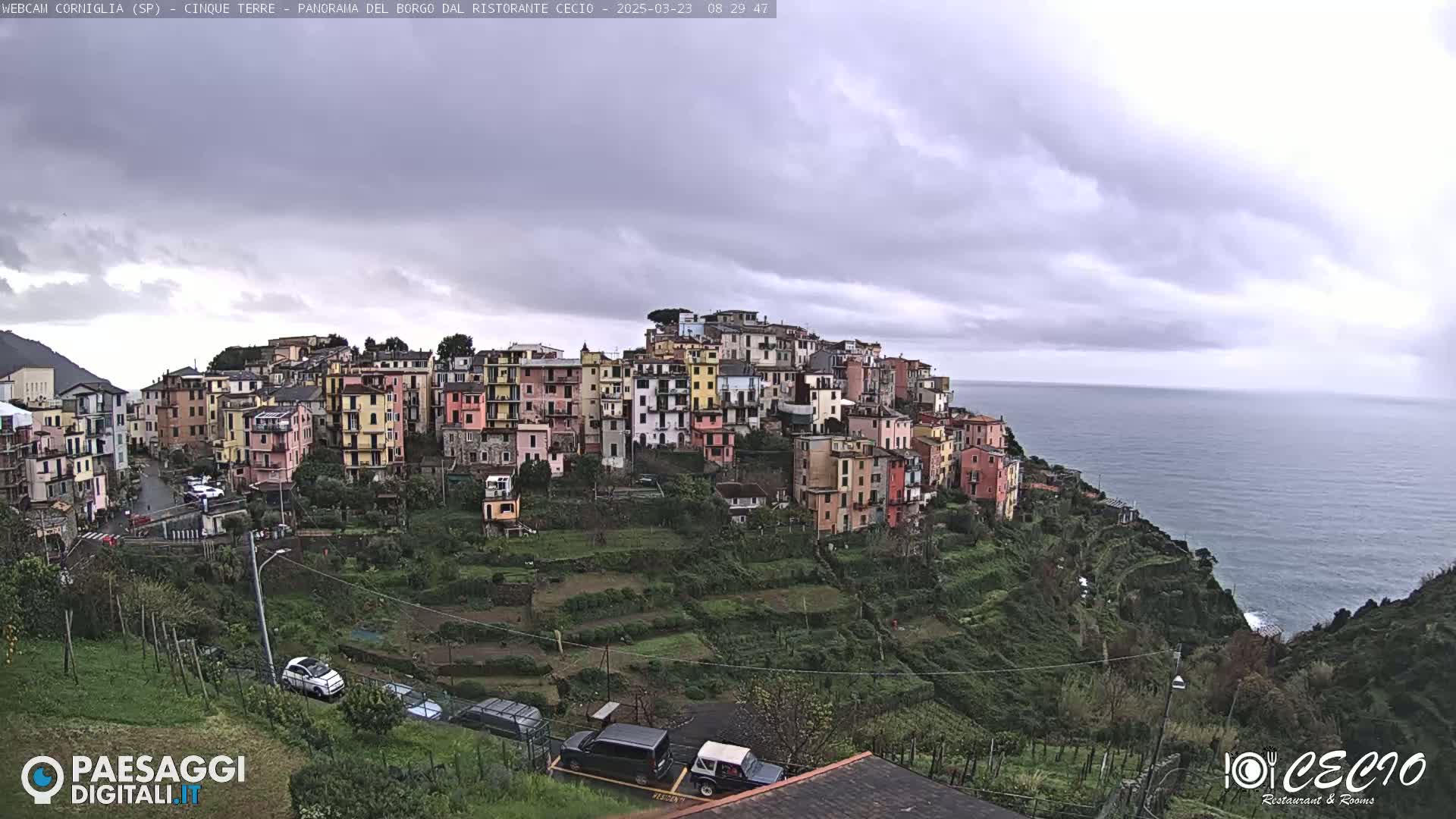 A colorful hillside village overlooks a calm ocean under an overcast sky.