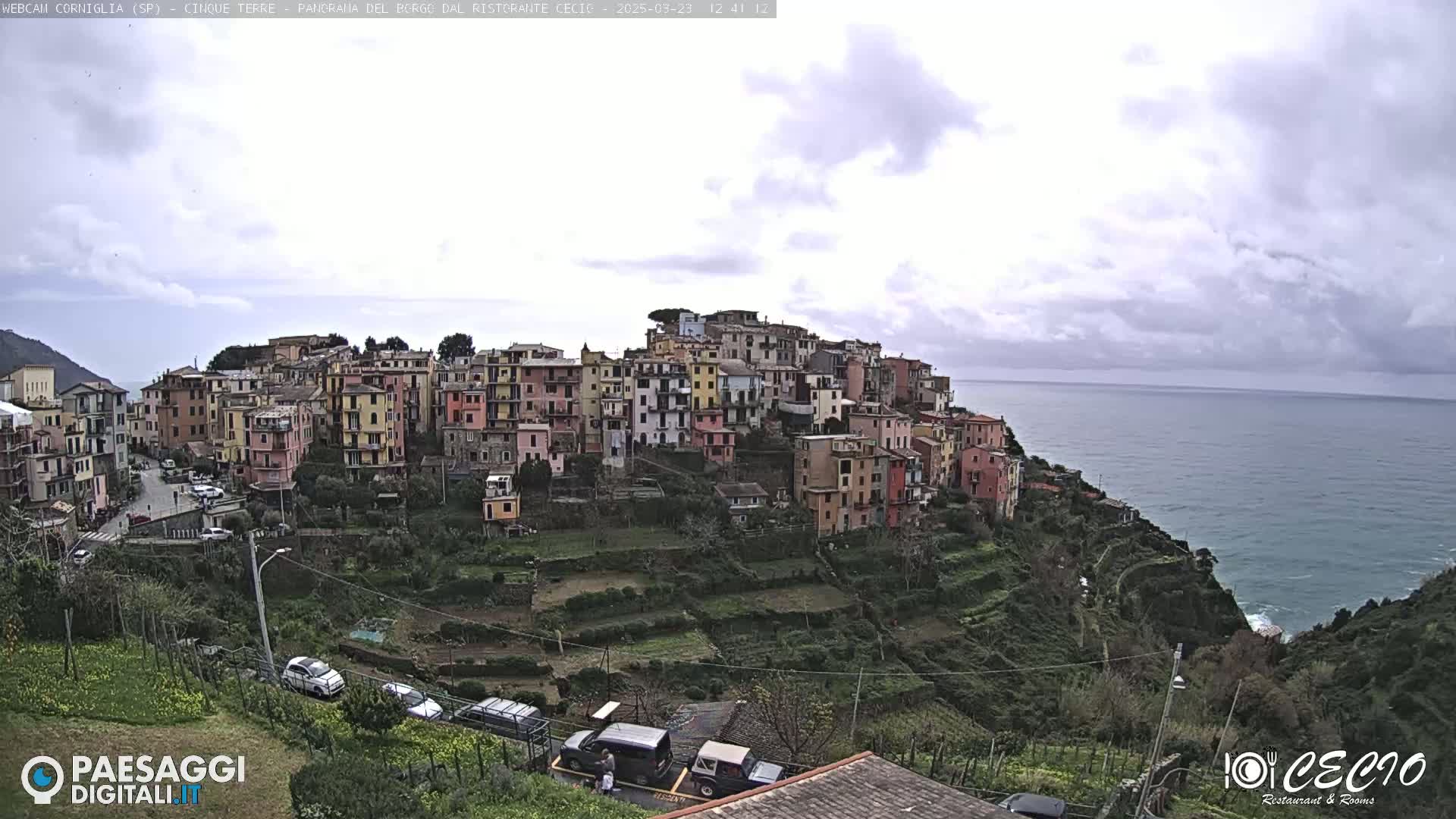 A coastal village of colorful buildings on a hillside overlooking a calm sea under a cloudy sky.