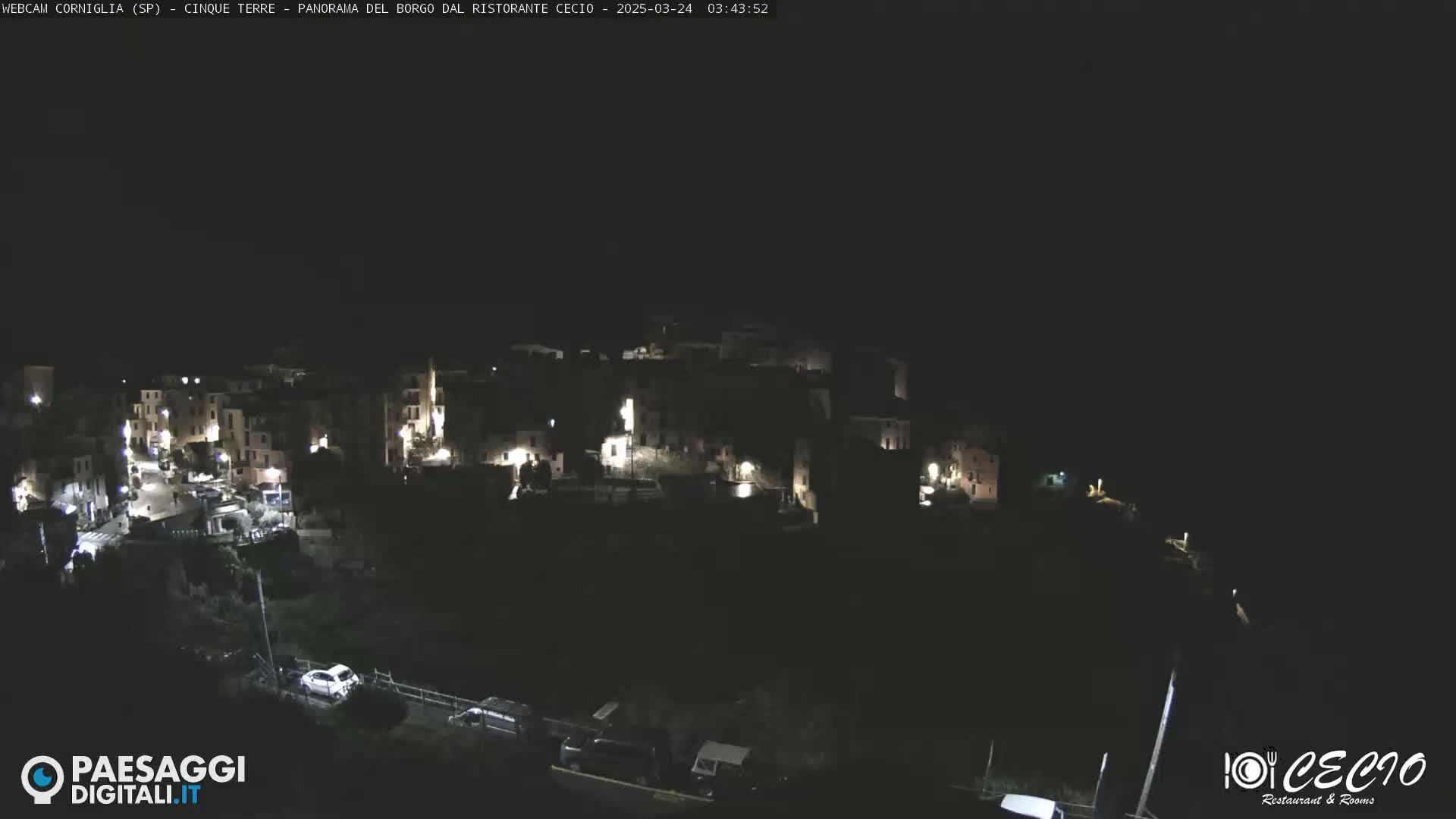 A nighttime, high-angle view of a small, illuminated town nestled on a hillside.