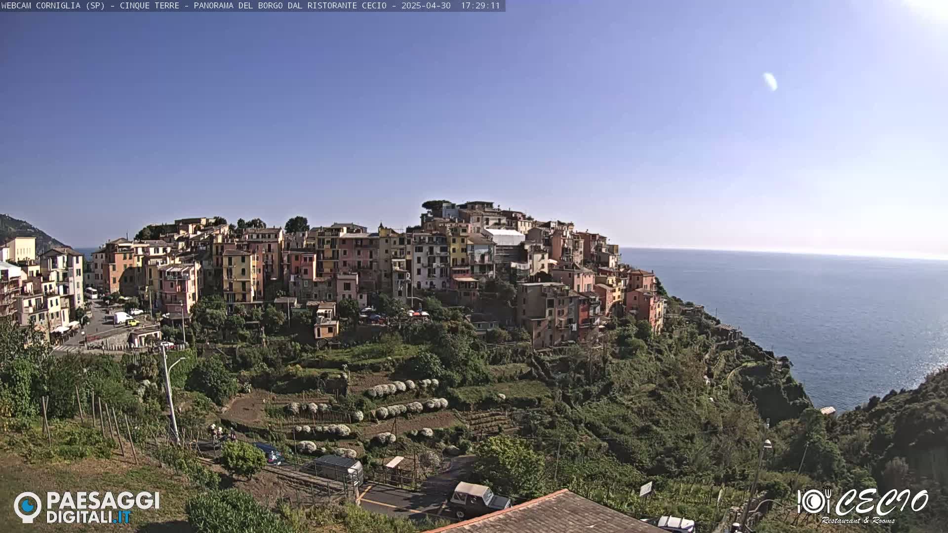A coastal village of colorful buildings on a hillside overlooks a calm blue sea under a clear, sunny sky.