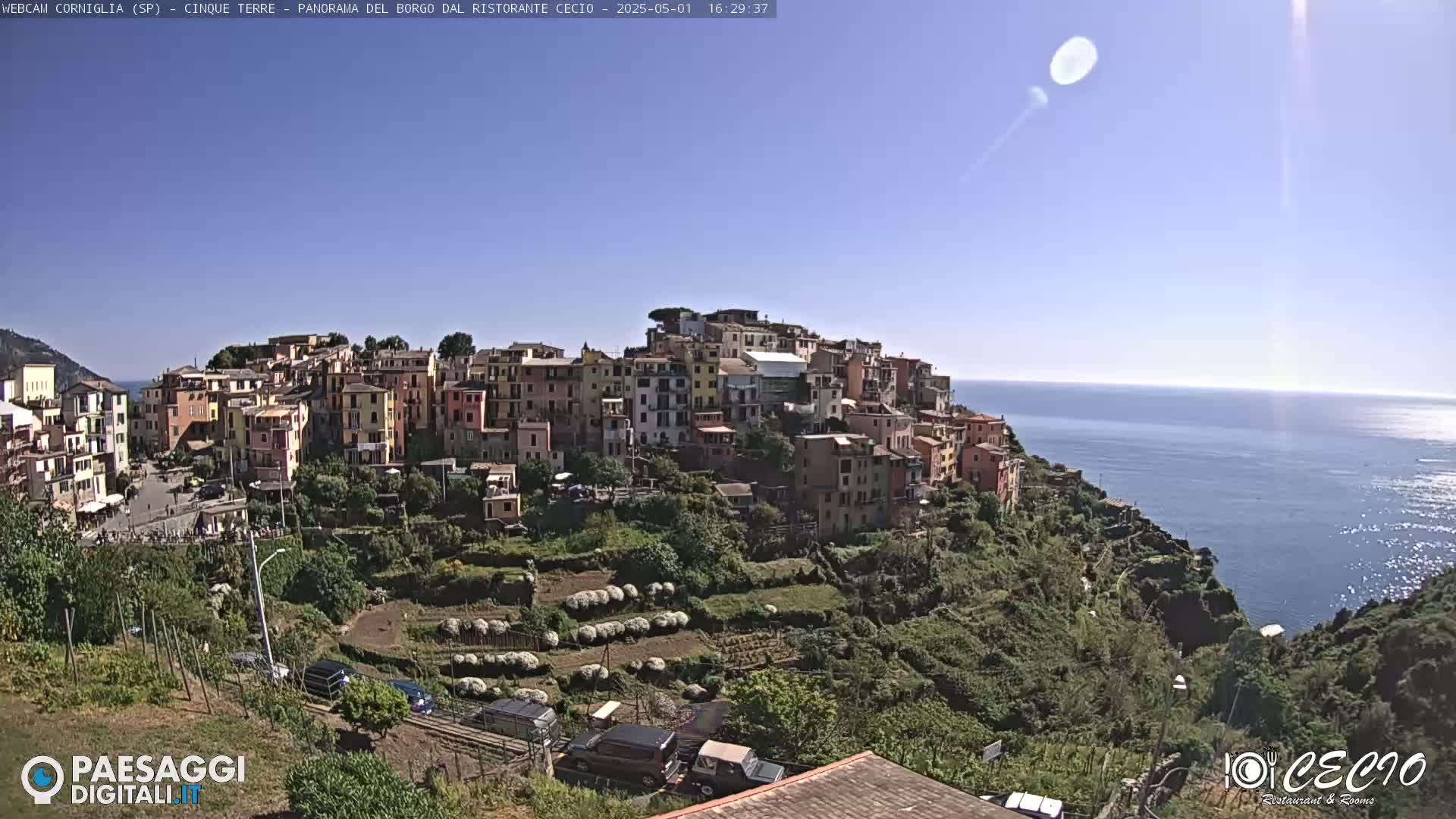 A colorful hillside village overlooks a calm blue ocean under a clear, sunny sky.