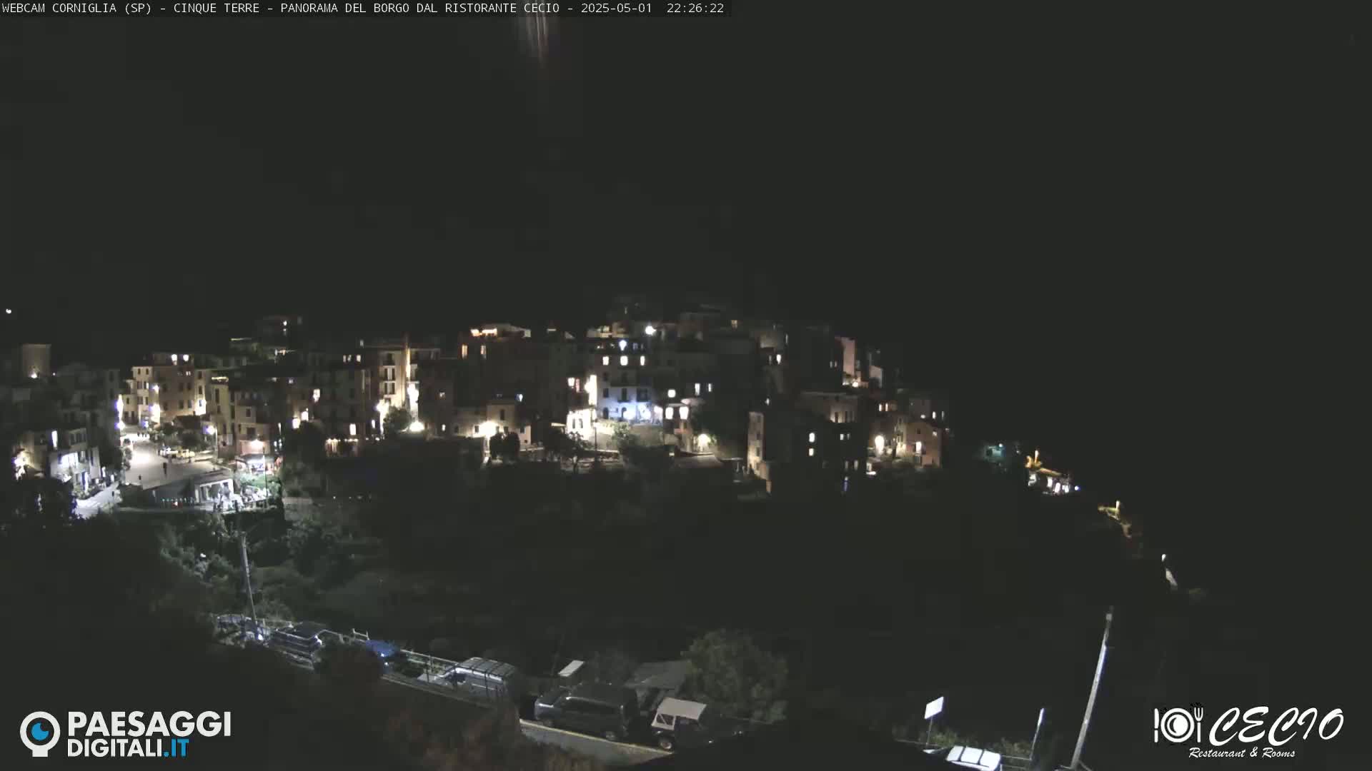 A nighttime, high-angle view of a small, illuminated village nestled on a hillside.