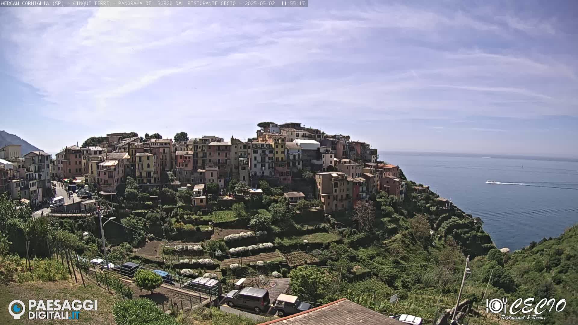 A colorful hillside village overlooks a calm blue sea under a mostly sunny sky.
