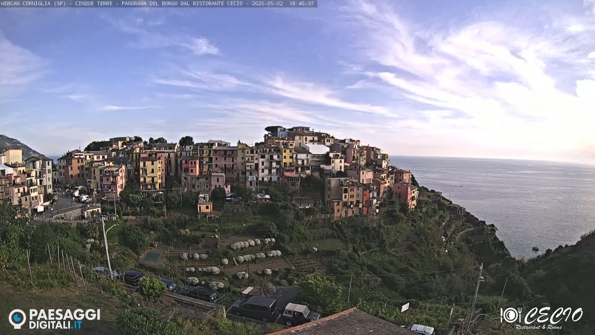 A colorful hillside village clings to a cliff overlooking a calm sea under a mostly clear, bright sky.