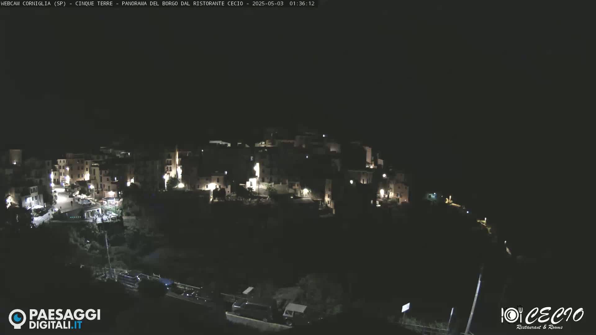 A nighttime, high-angle view shows a small, illuminated village nestled on a dark hillside.