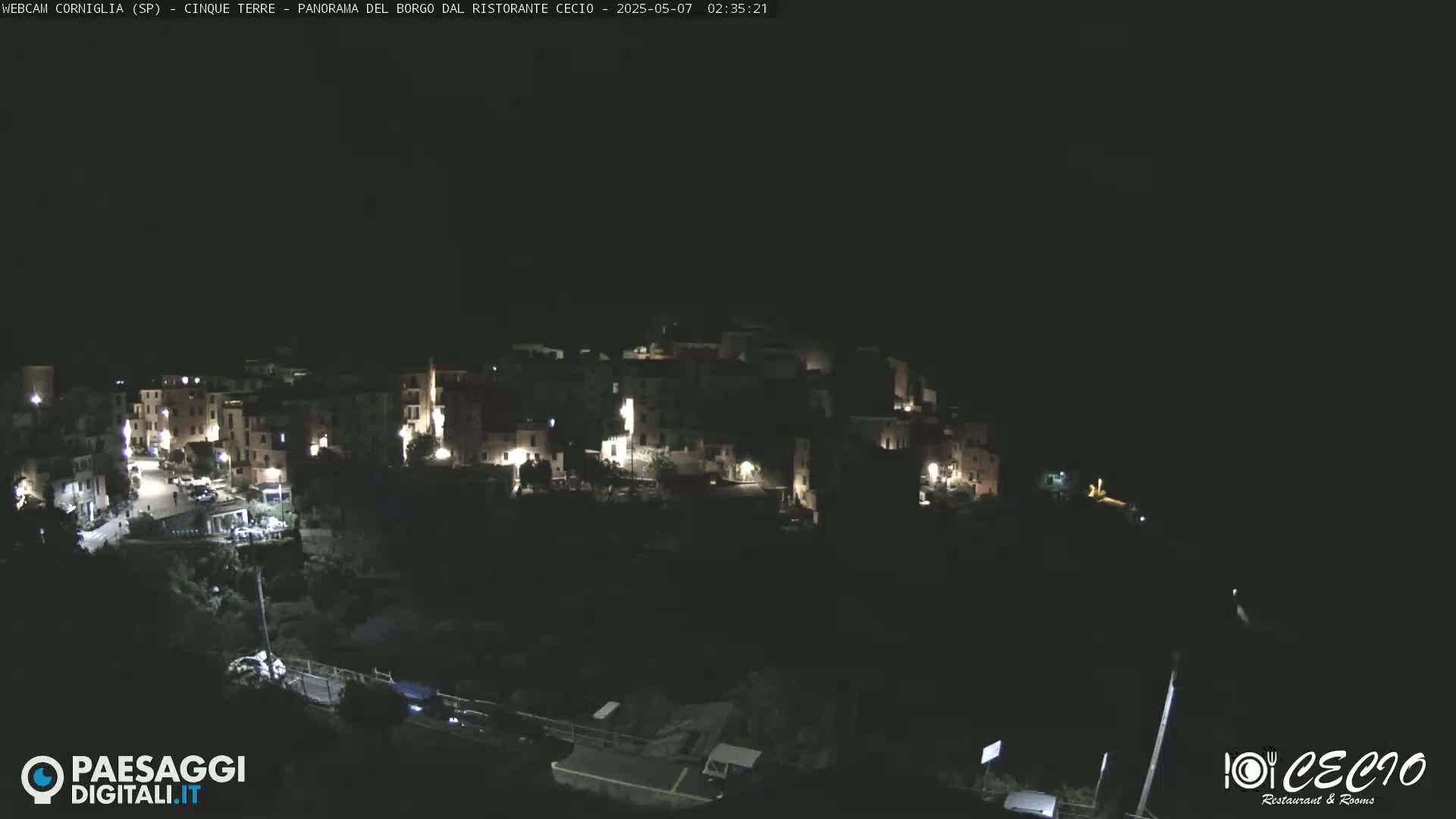 A nighttime, overhead view of a small, illuminated town nestled on a hillside under a dark sky.