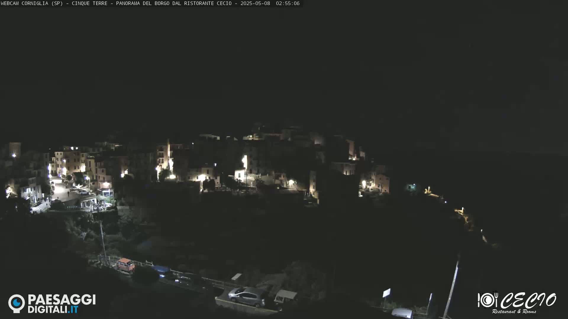 A nighttime, aerial view of a small, illuminated village nestled on a dark hillside.