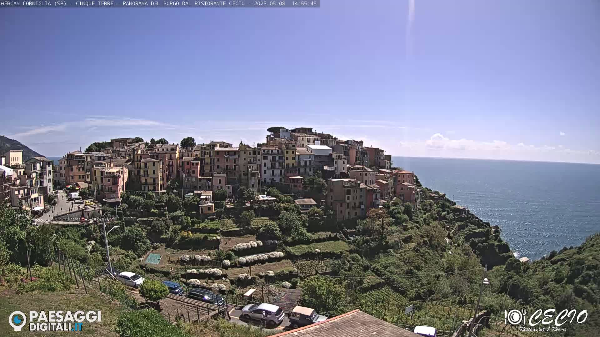 A colorful hillside village overlooks a calm blue sea under a mostly clear sky.