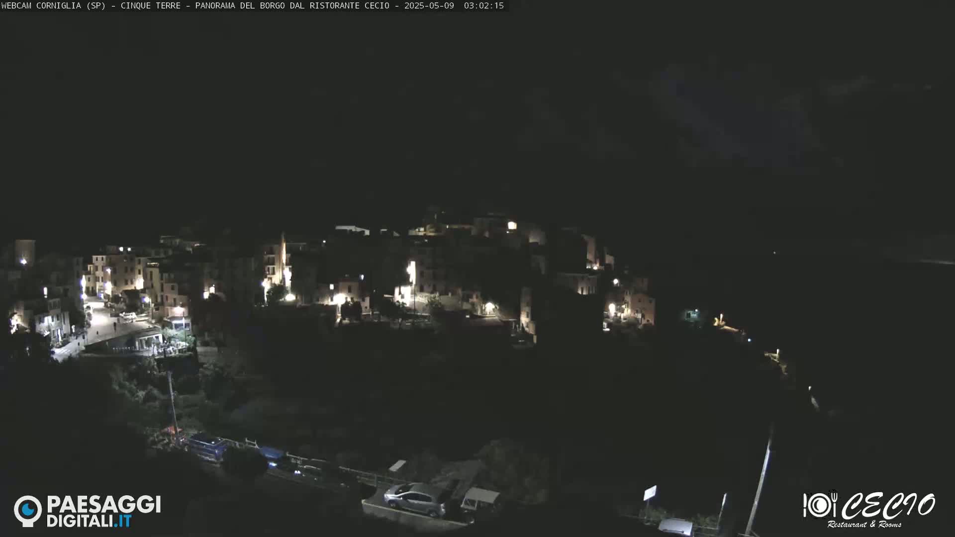 A nighttime aerial view of a small, dimly lit town nestled on a hillside.