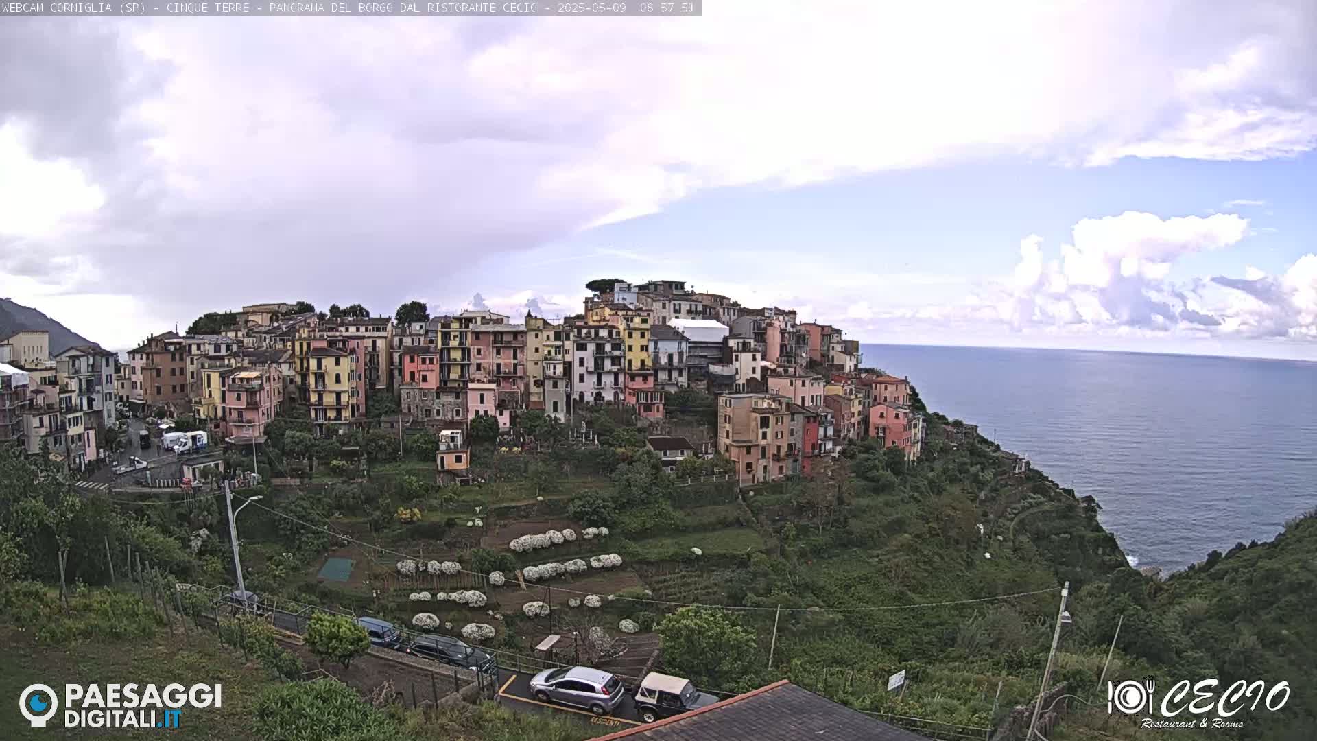 A colorful hillside village overlooks a calm ocean under a partly cloudy sky.