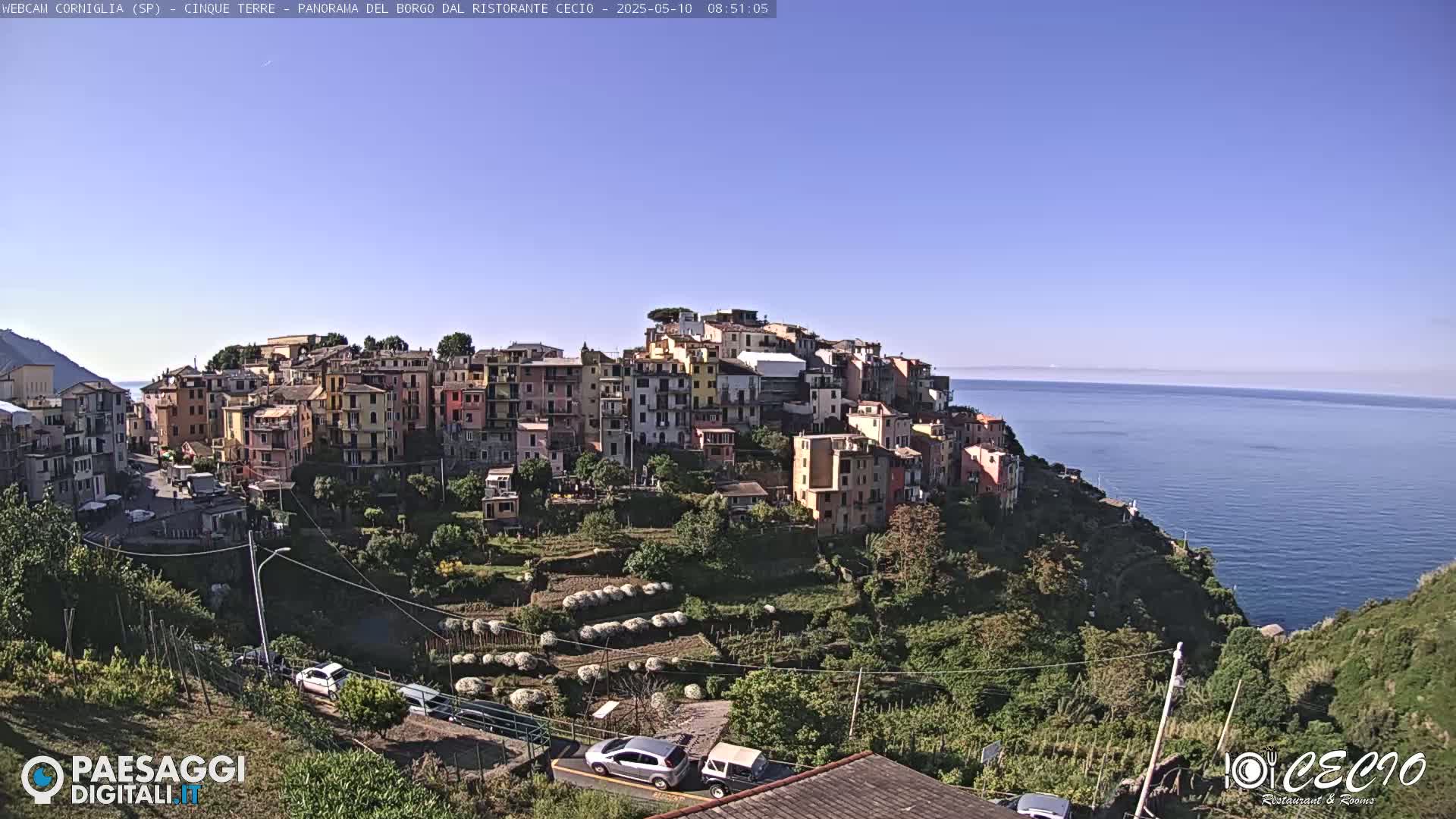 A colorful hillside village overlooks a calm blue sea under a clear, sunny sky.