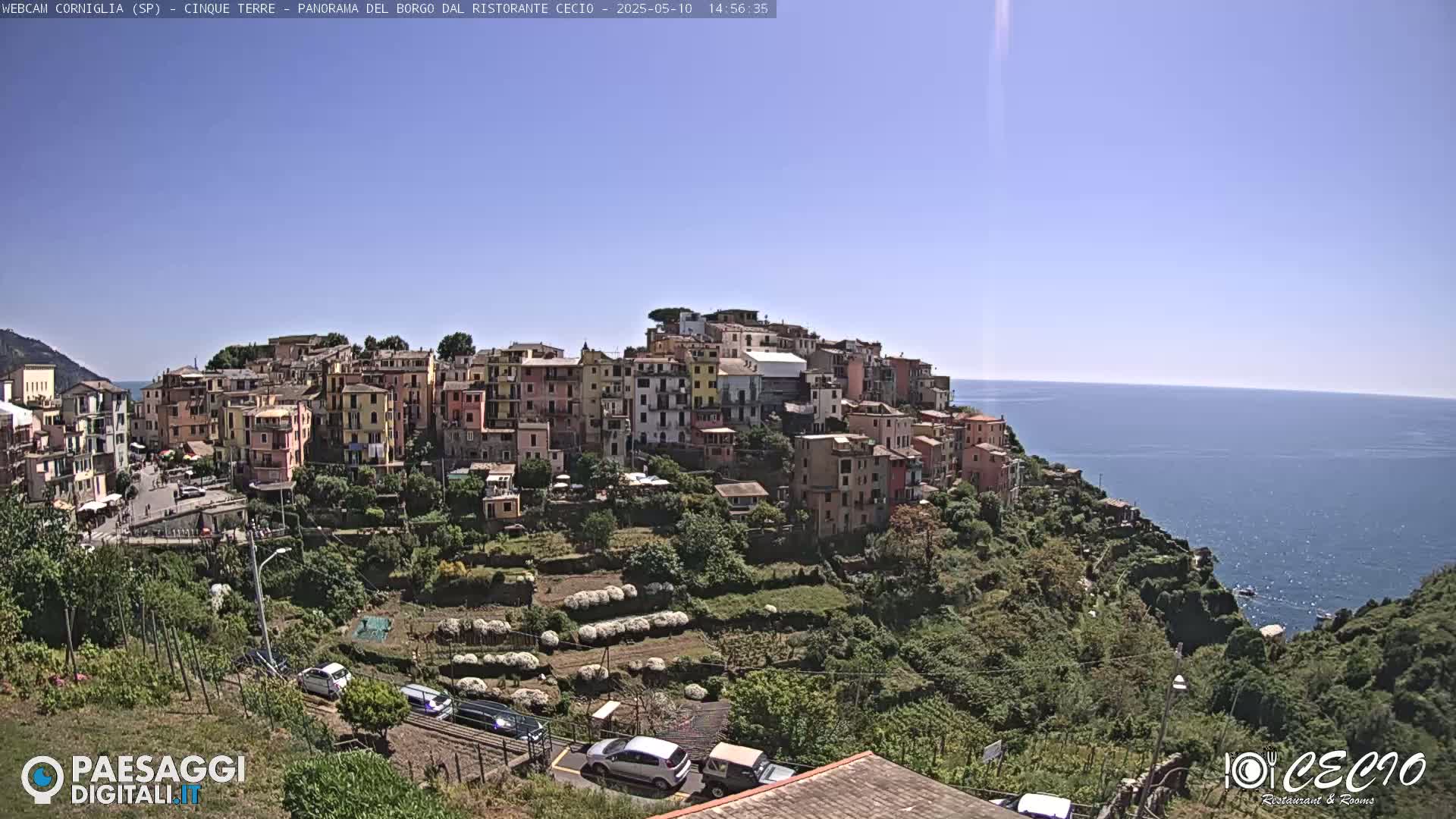 A colorful village clings to a hillside overlooking a calm blue sea under a clear, bright sky.