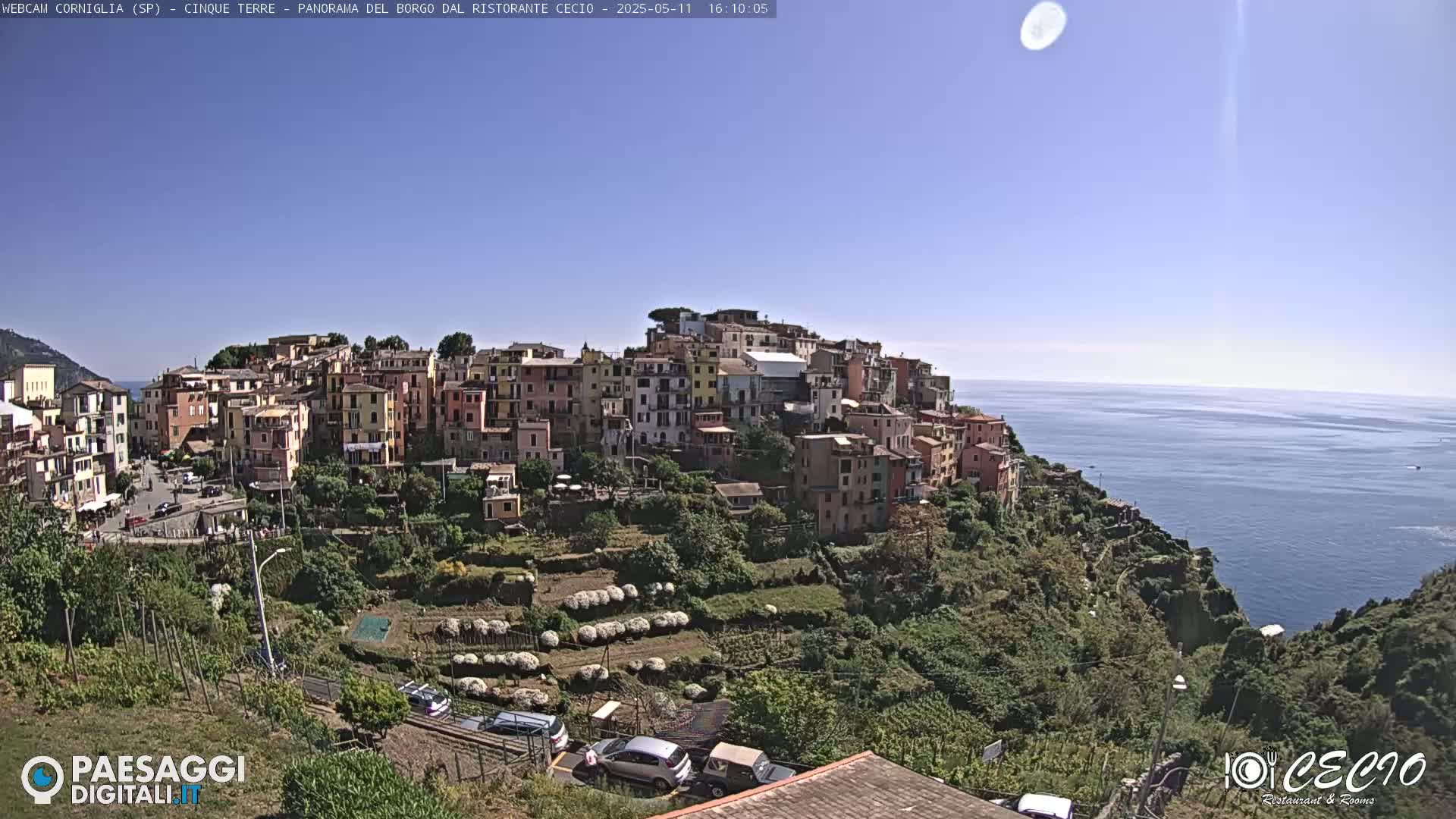 A colorful hillside village overlooks a calm blue ocean under a clear, sunny sky.