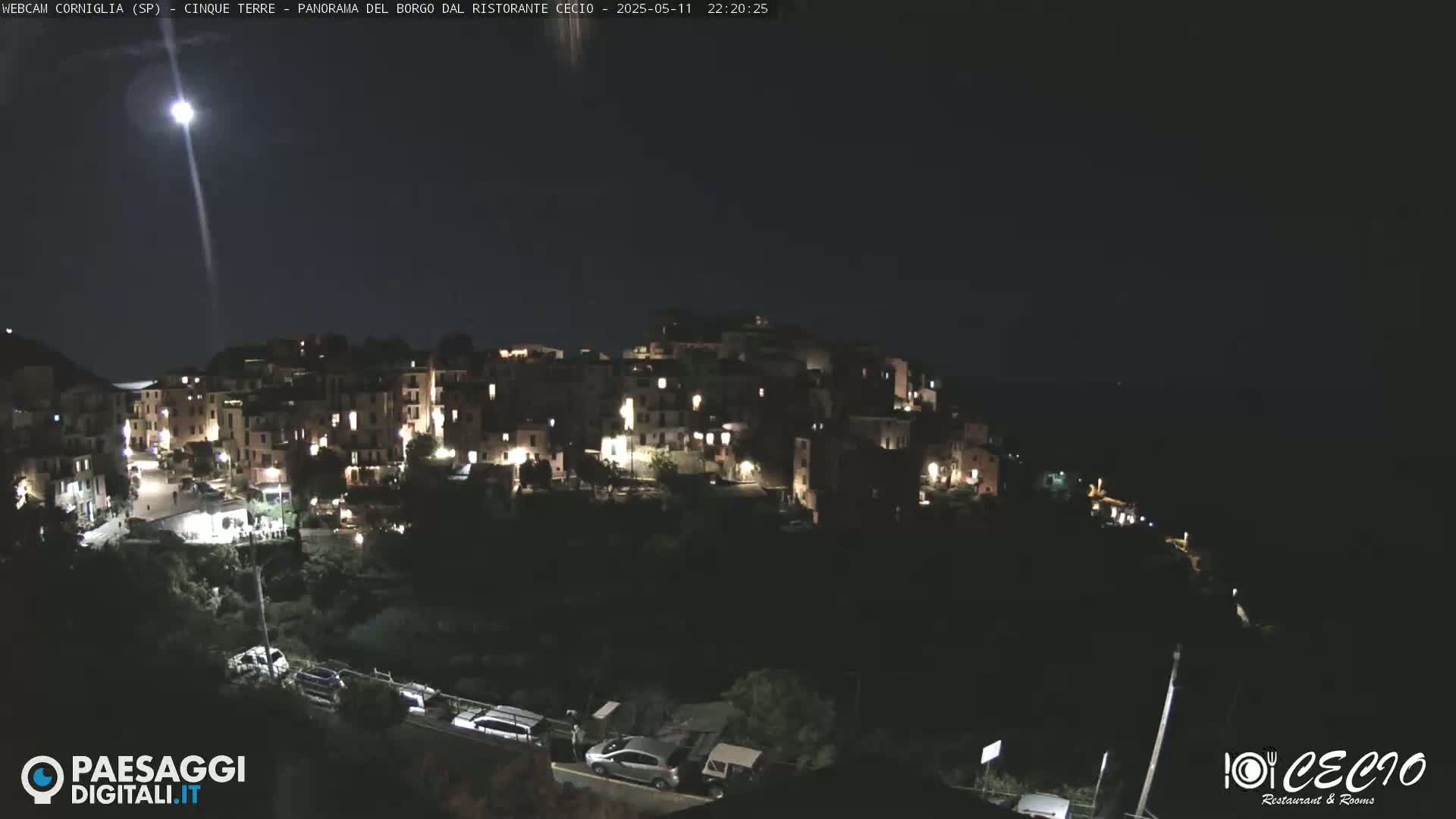 A nighttime, moonlit view of a small, illuminated village nestled on a hillside.
