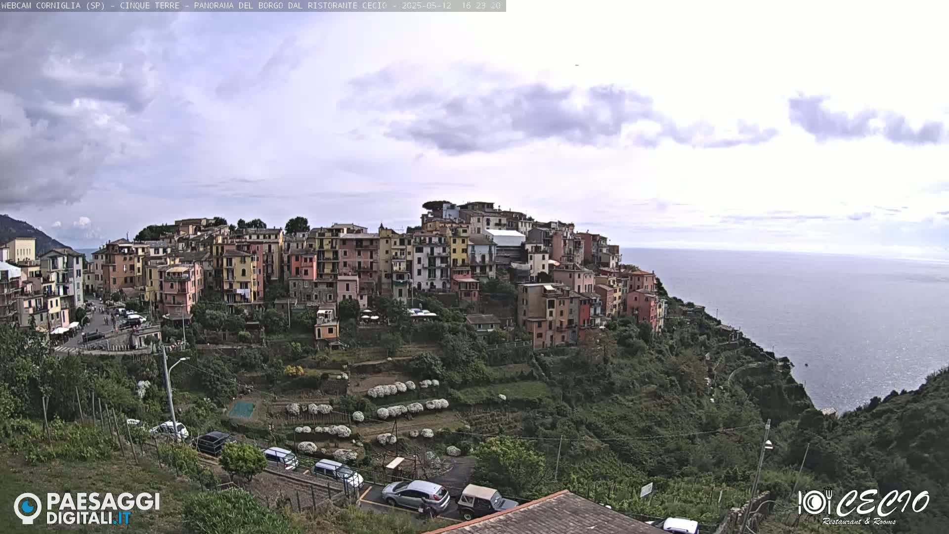 A coastal village of colorful buildings on a hillside overlooking a calm sea under a partly cloudy sky.
