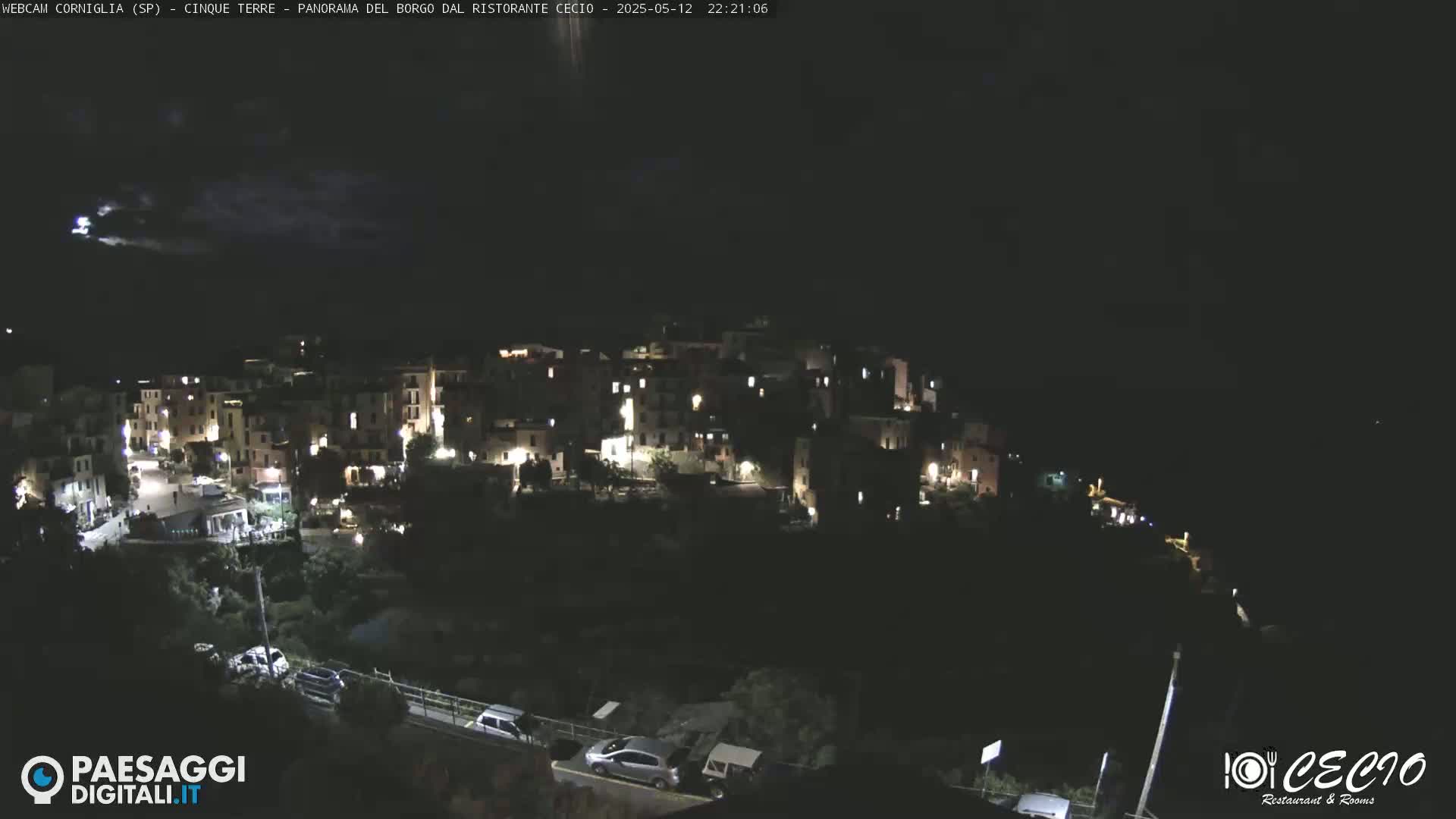 A nighttime view of a small, illuminated village nestled on a hillside under a dark, cloudy sky.