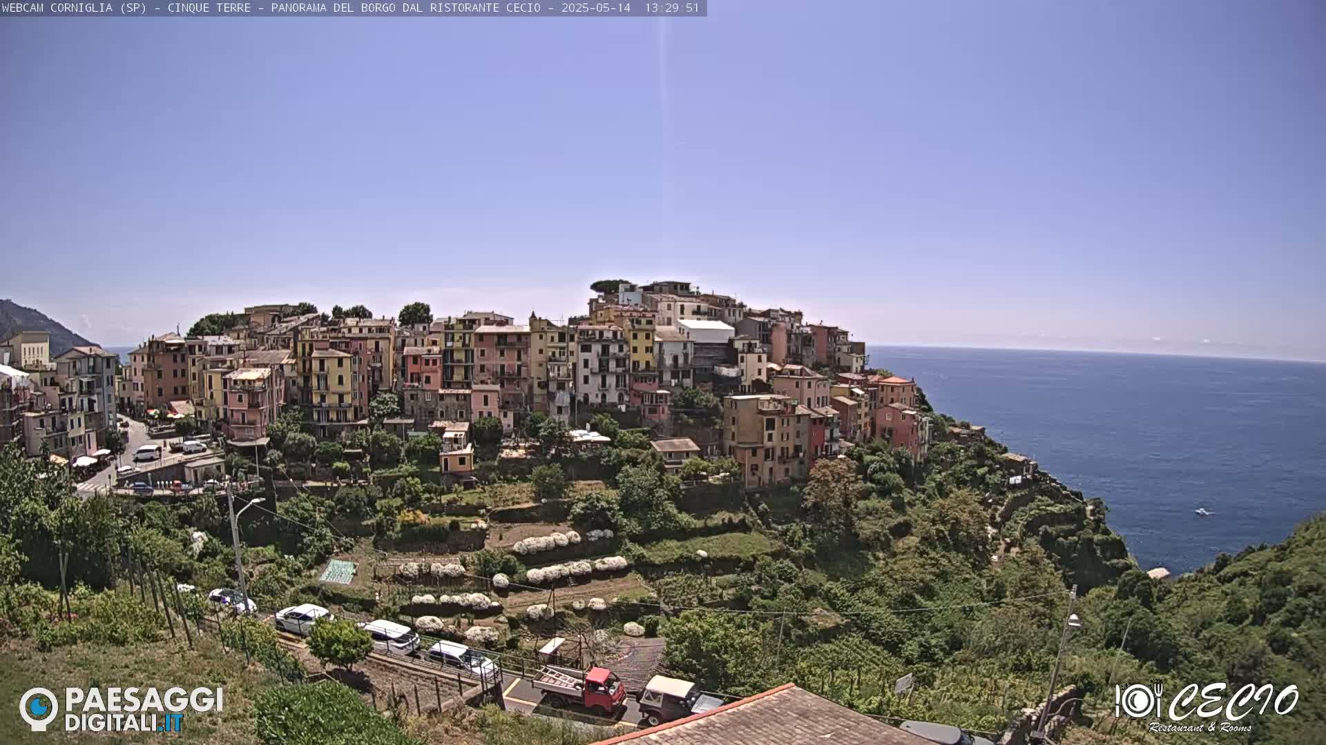 A colorful hillside village overlooks a calm blue sea under a clear sky.