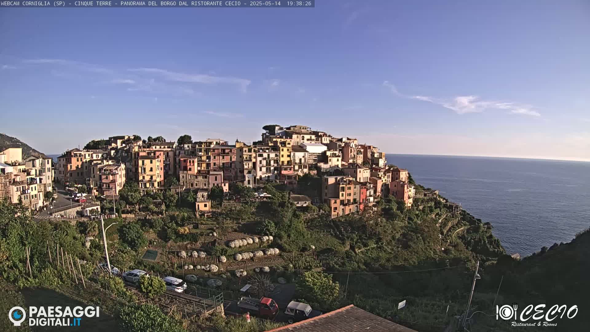 A colorful village clings to a hillside overlooking a calm sea under a clear blue sky.
