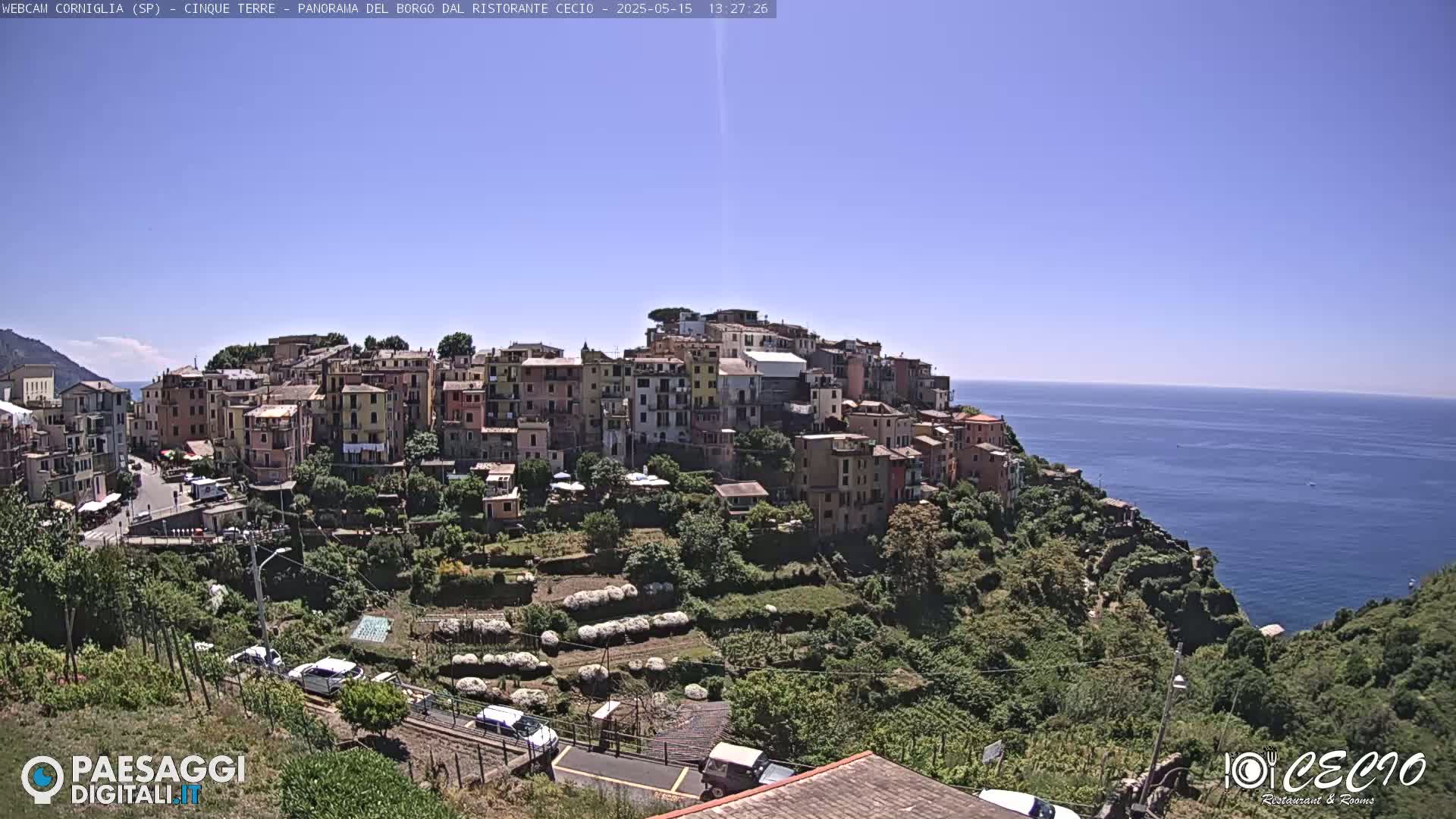 A coastal village of colorful buildings climbs a hillside overlooking a calm blue sea under a clear blue sky.