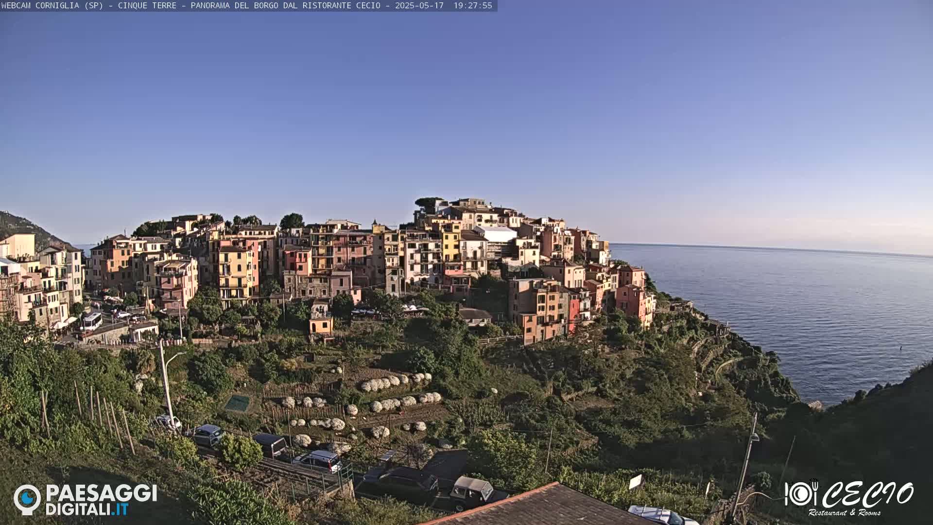 A colorful hillside village overlooks a calm ocean under a clear blue sky.