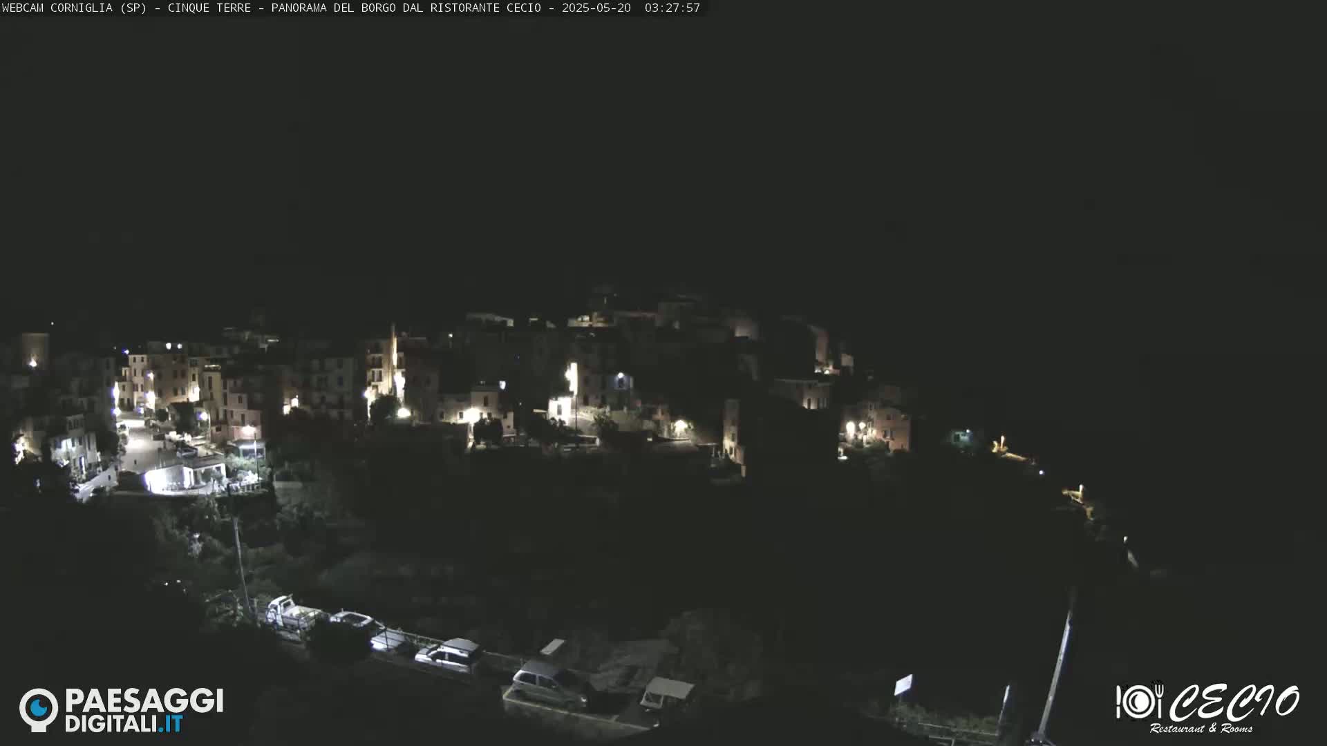 A nighttime, high-angle view of a small, dimly lit village nestled on a hillside.