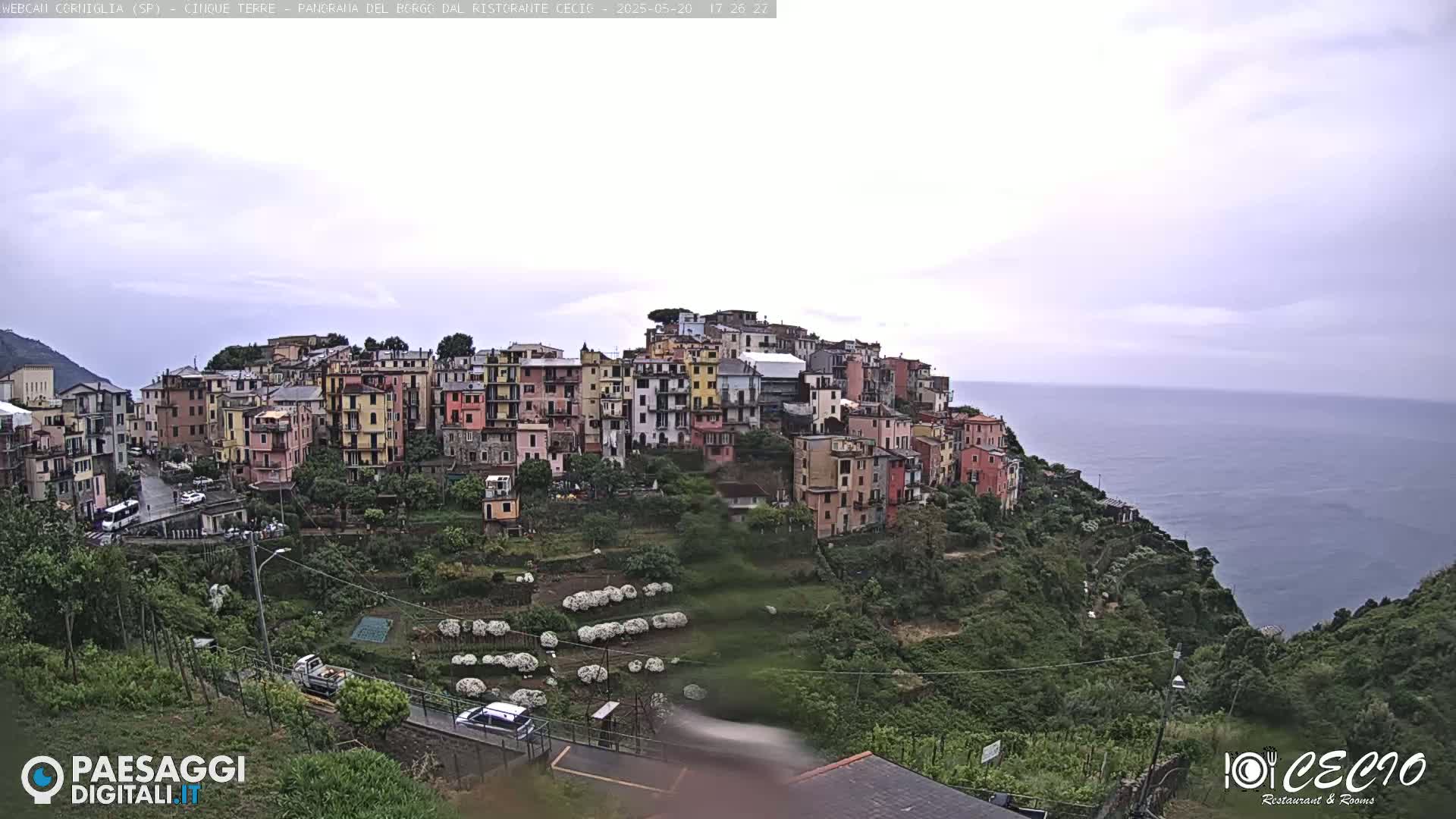 A colorful hillside village overlooks a calm sea under an overcast sky.