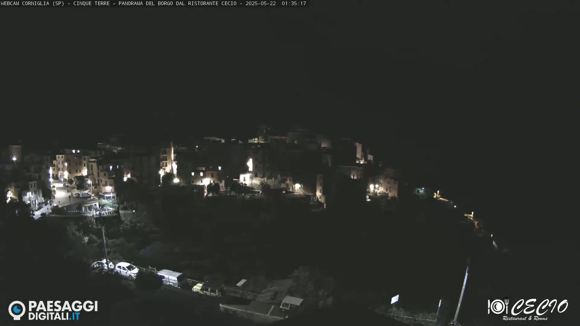 A nighttime, aerial view of a small, illuminated village nestled on a hillside.