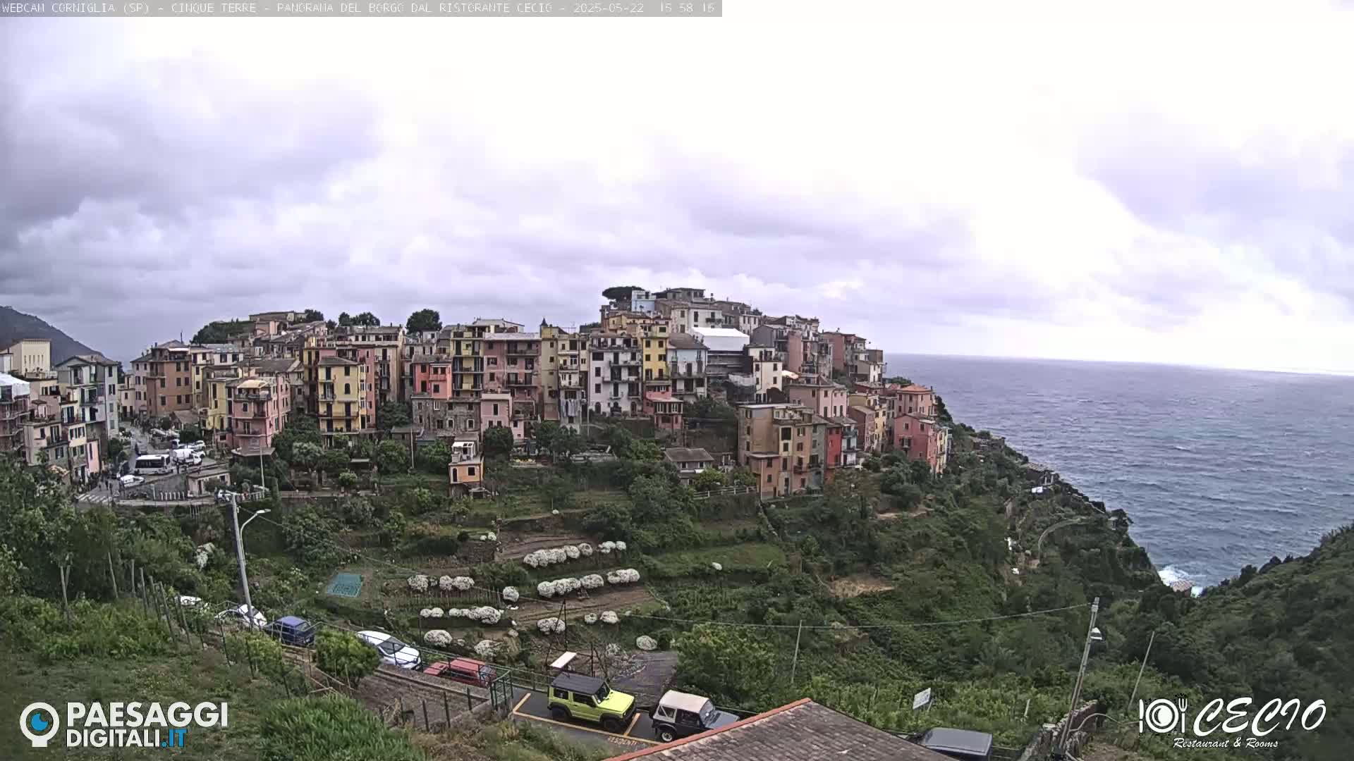 A colorful hillside village overlooks a calm sea under an overcast sky.