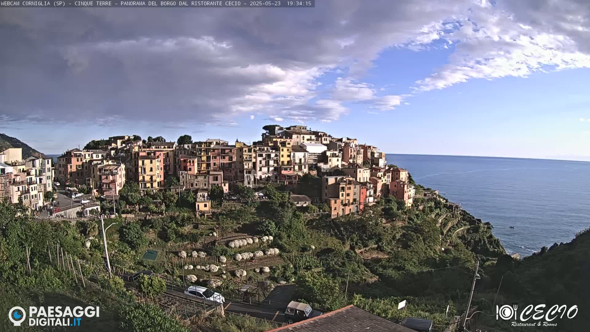 A coastal village of colorful buildings clings to a hillside overlooking a calm sea under a partly cloudy sky.