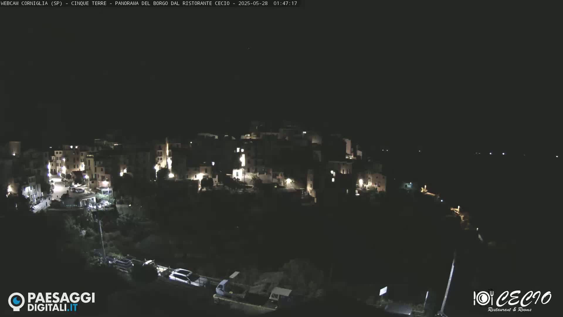 A nighttime, overhead view of a small, hilly town with scattered lights, under a clear, dark sky.