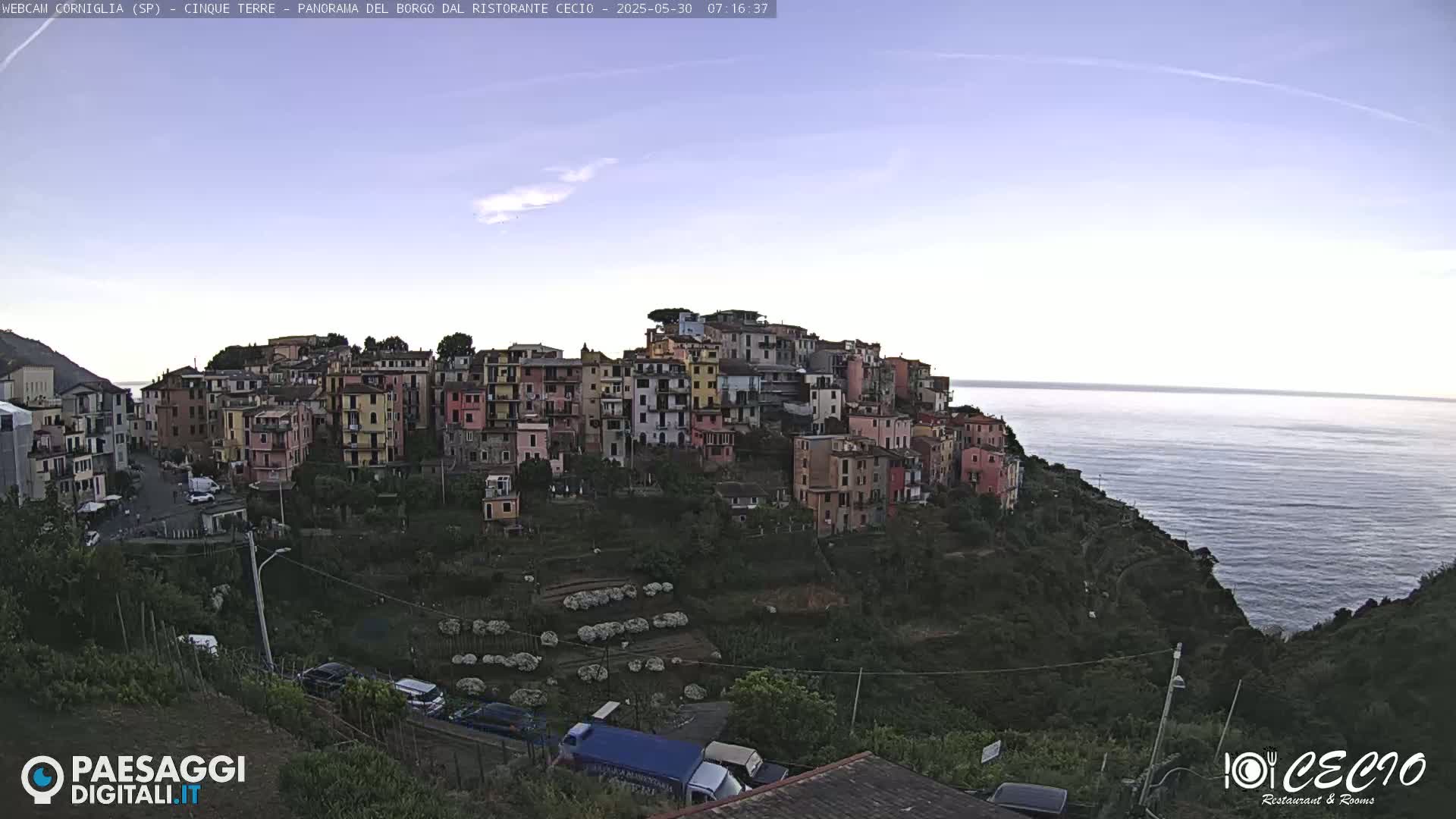 A colorful hillside village overlooks a calm sea under a clear, light-blue sky.