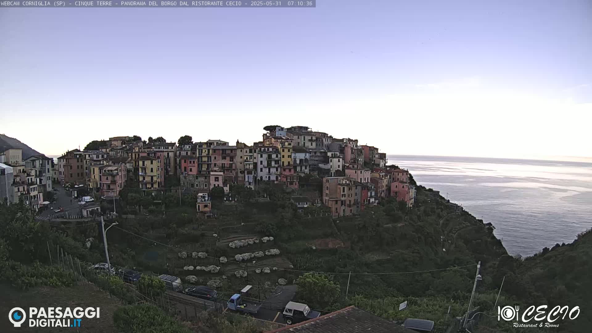 A colorful hillside village overlooks a calm sea under a clear, twilight sky.
