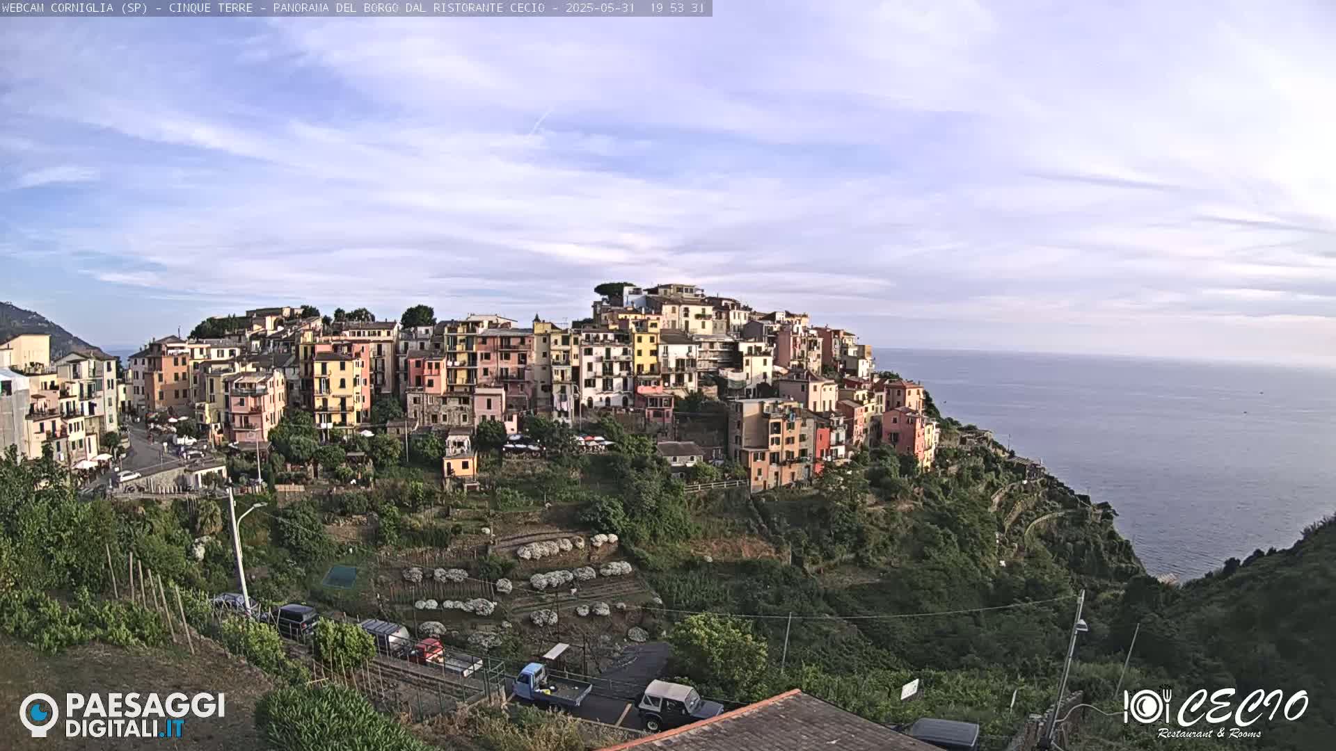 A colorful hillside village overlooks a calm ocean under a mostly clear sky.