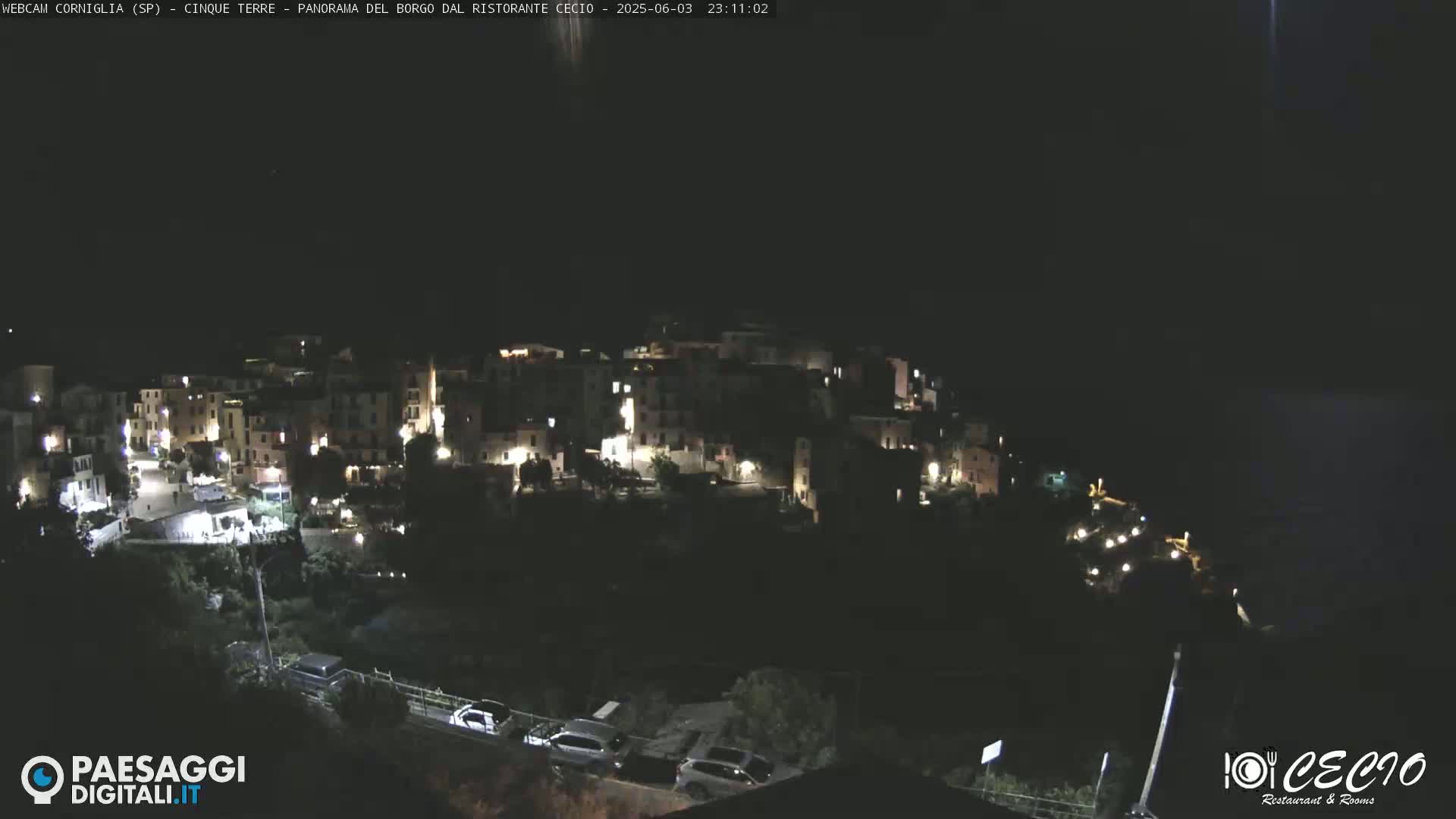 A nighttime, high-angle view shows a small, illuminated town nestled on a hillside.