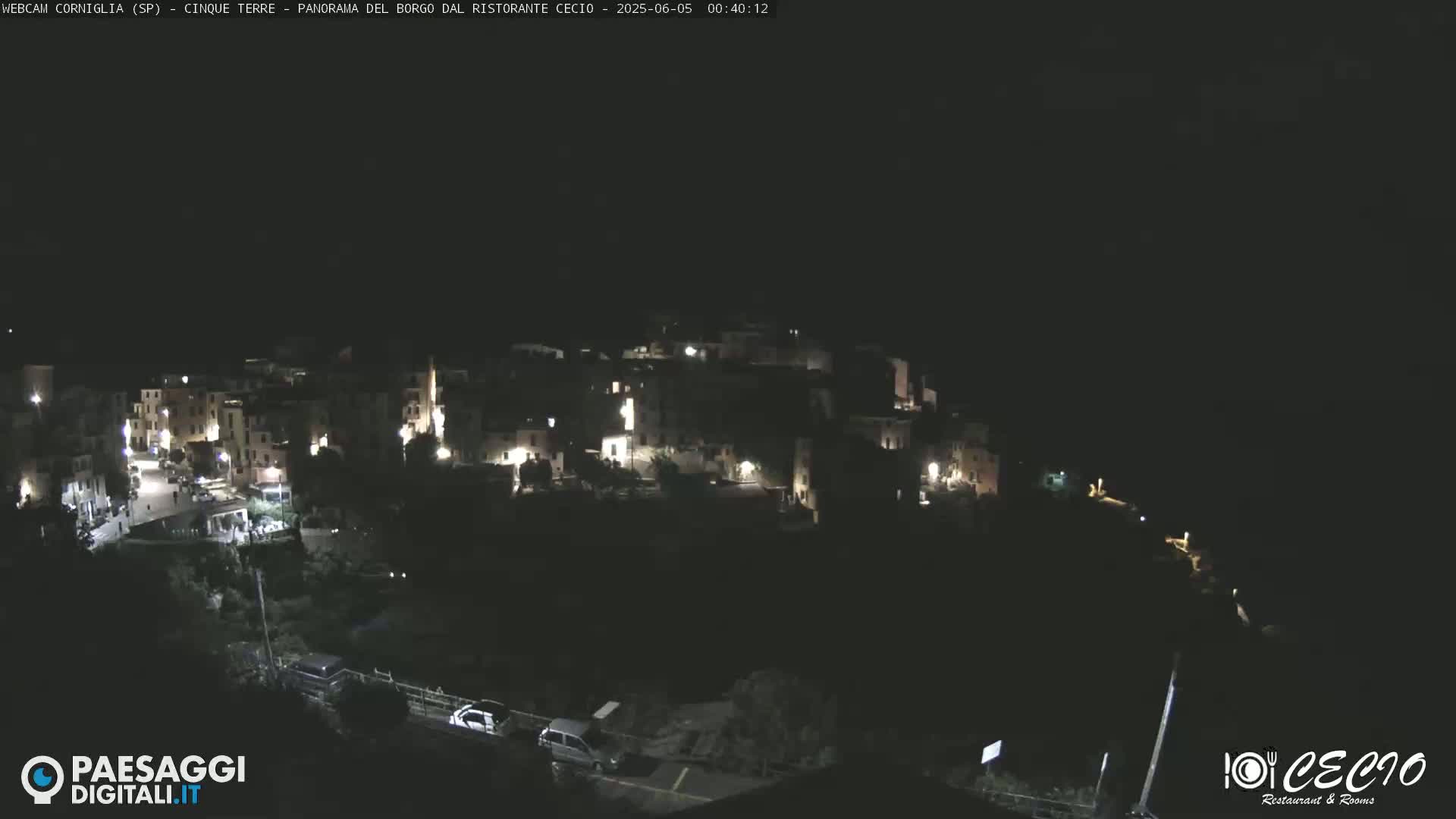 A nighttime, aerial view of a small, illuminated village nestled on a hillside.