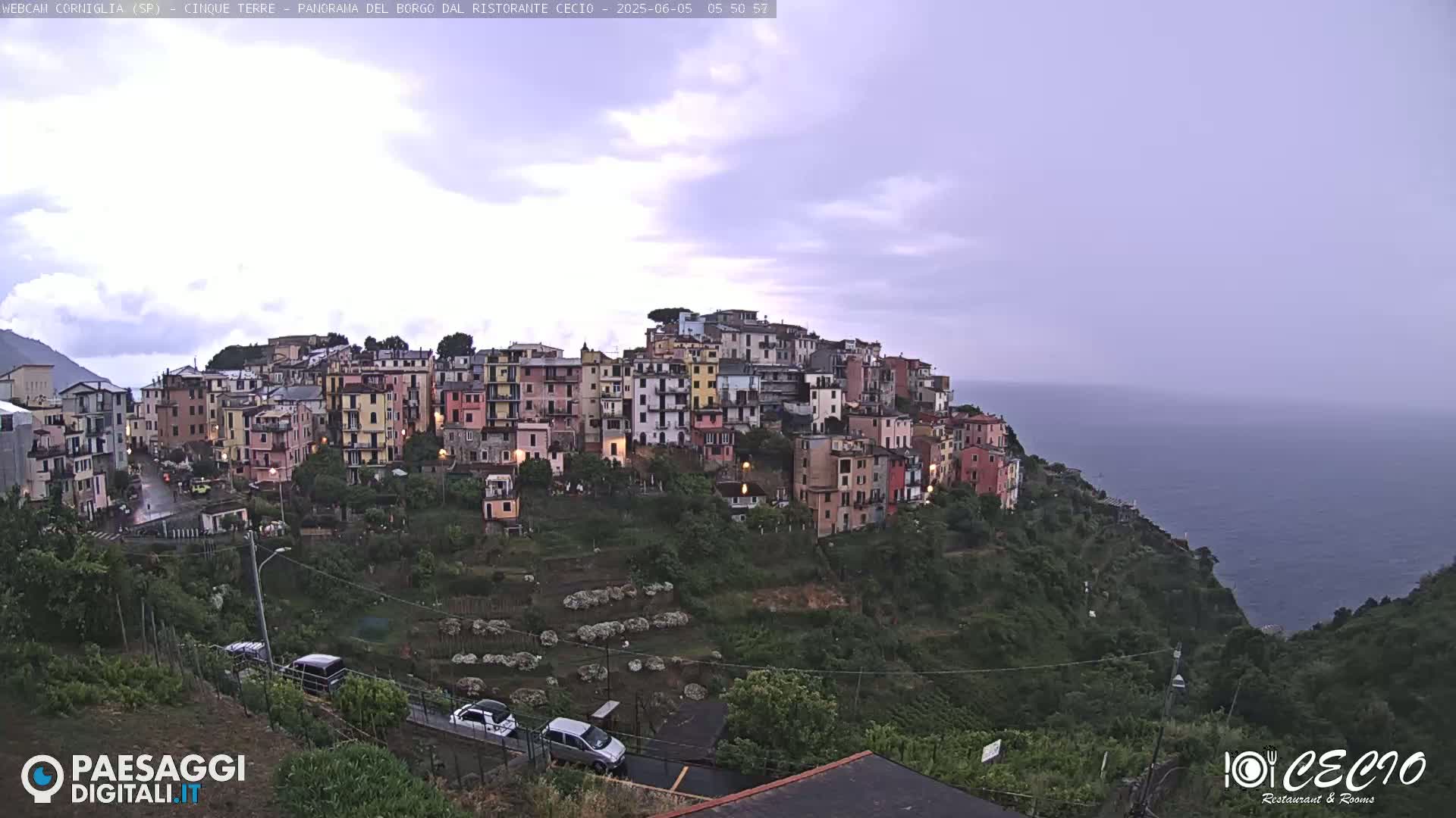 A colorful hillside village overlooks a calm sea under an overcast sky.