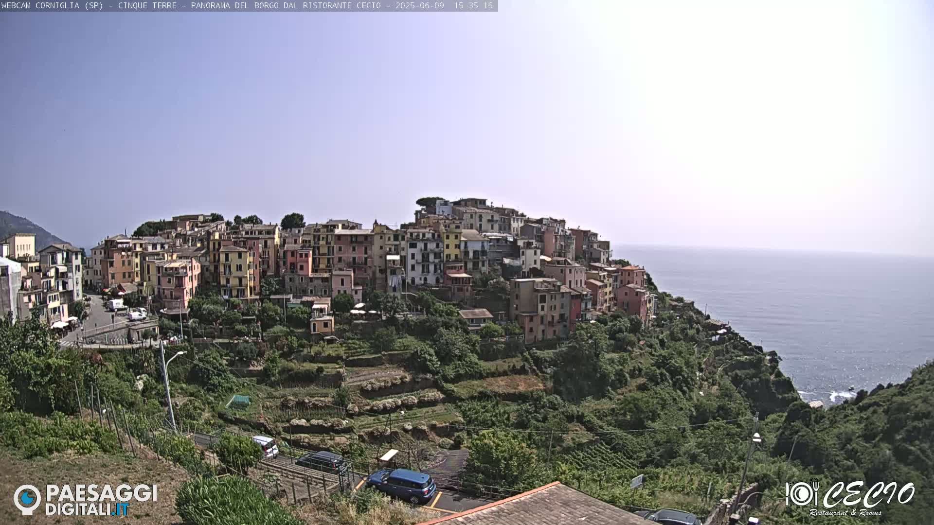 A hillside village of colorful buildings overlooks a calm ocean under a clear, bright sky.